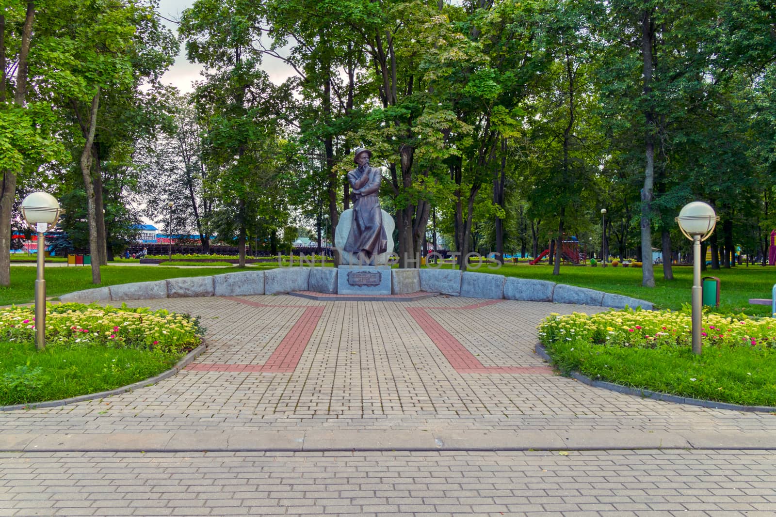 Bronze monument in the middle of the park with decorative flower beds and lanterns on the sides