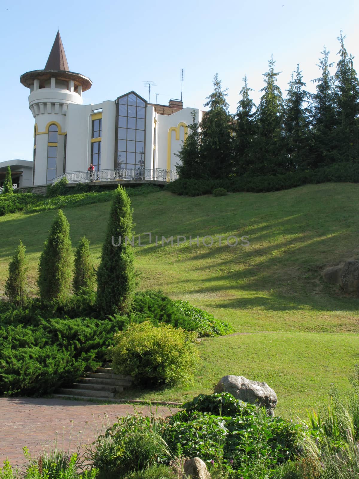 A steep green slope with a trimmed lawn and trees leading from a modern building with large windows