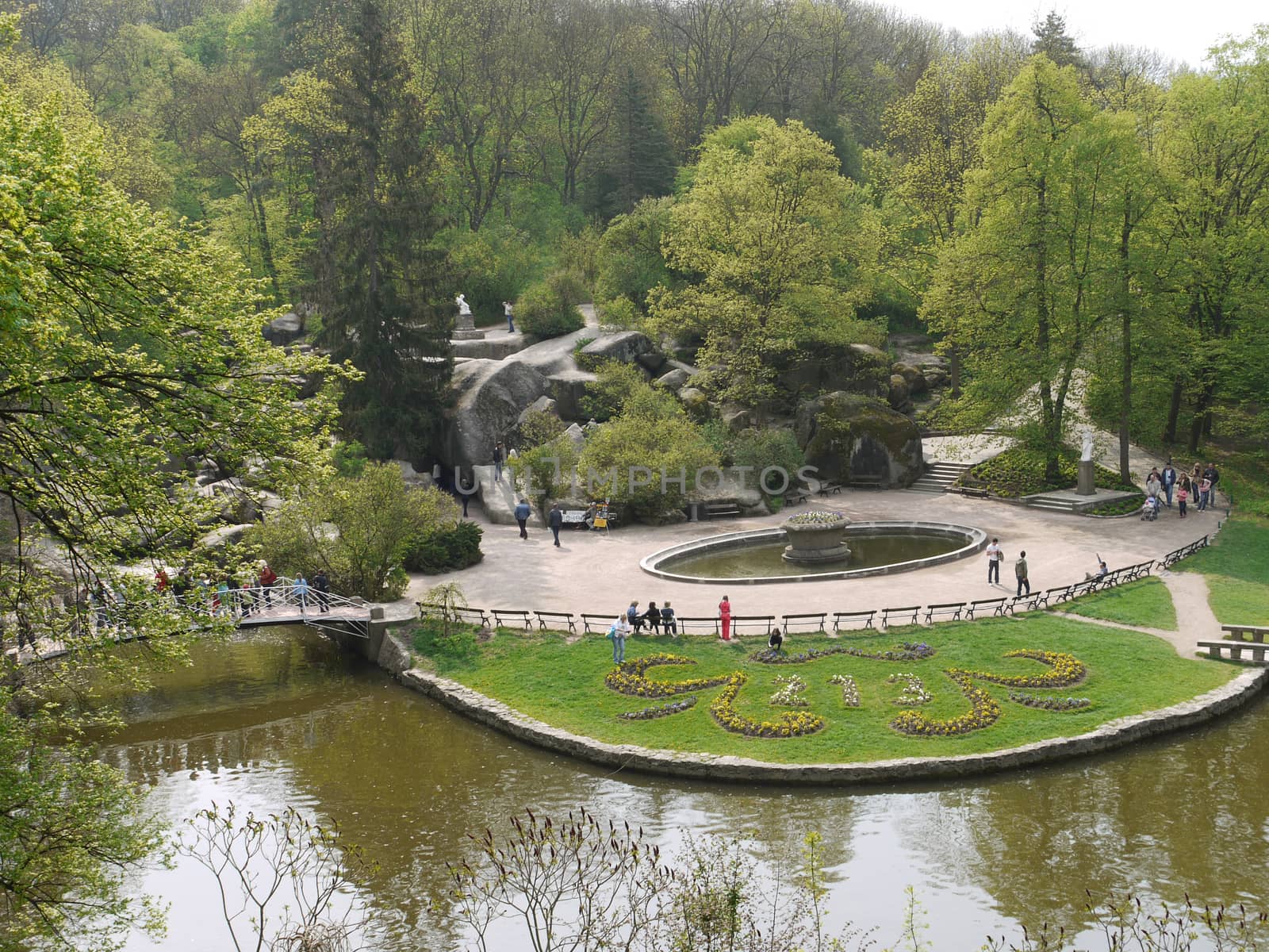 A large number of tourists stroll through the park with green decorative lawns, lakes with bridges and beautiful stone boulders