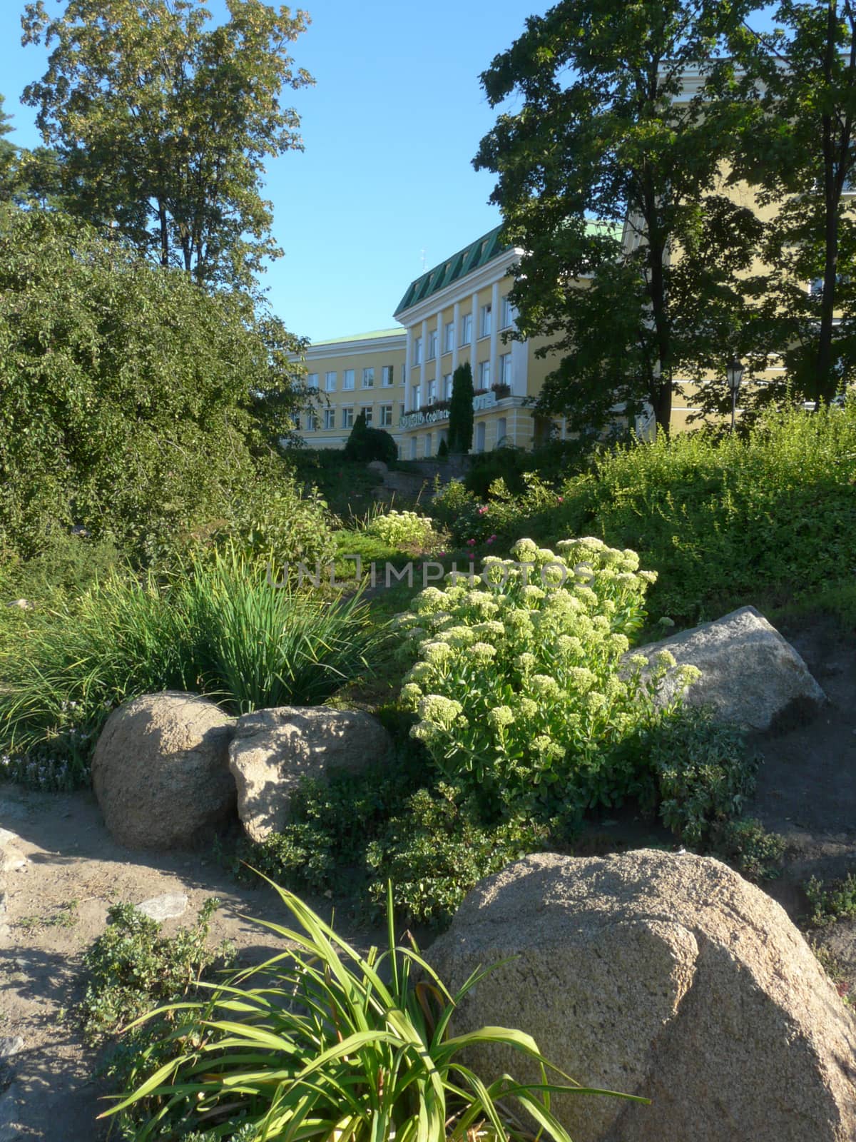 a rocky flowerbed with flowers and bushes near a large bright ho by Adamchuk