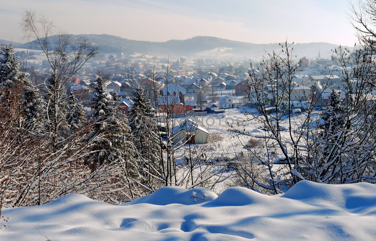 Carpathian town is covered with white snow in a valley of mountains with transparent fog