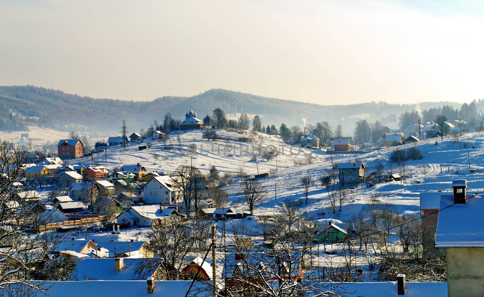 Rural settlement with small snow-covered houses, yards and a church on a hill