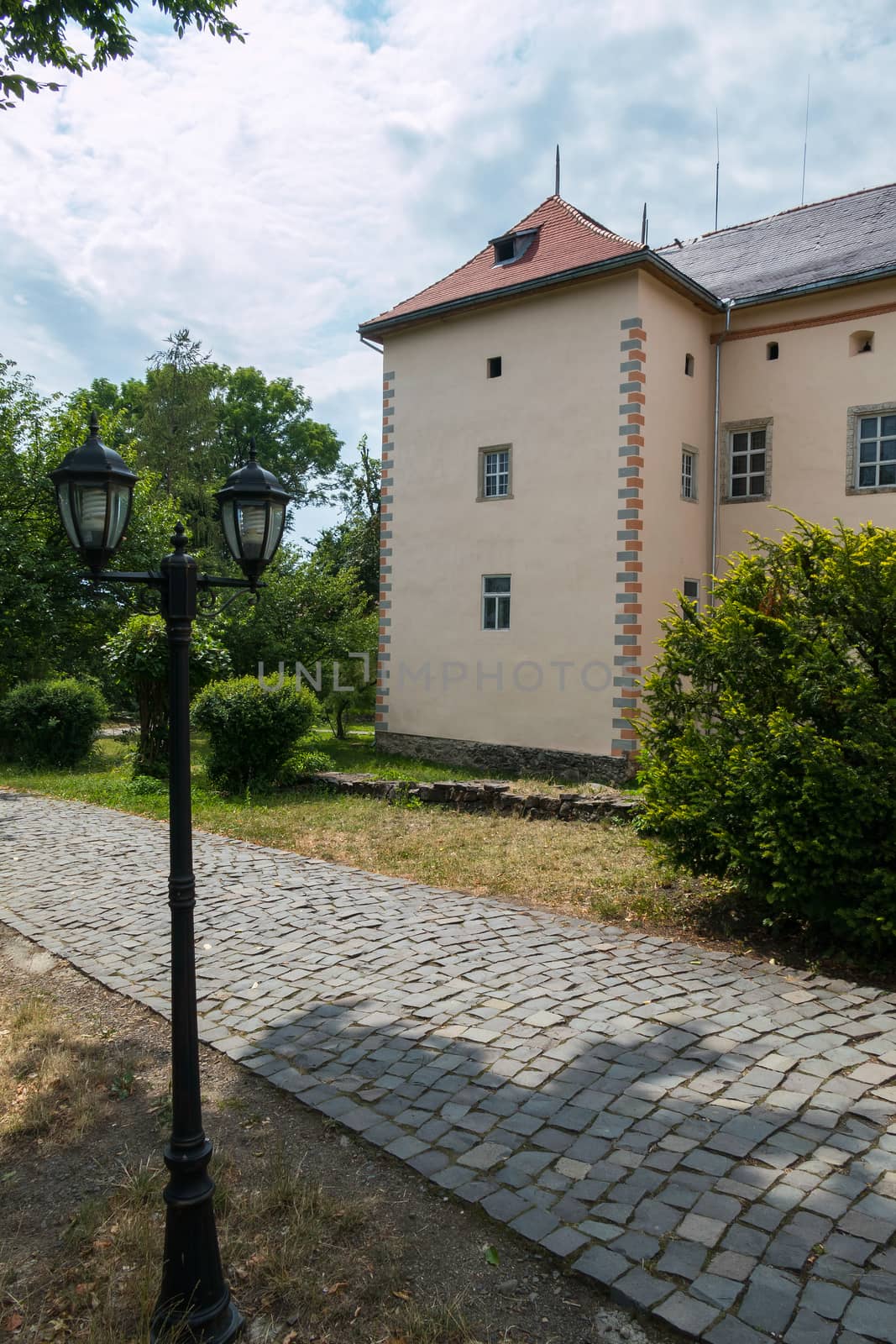 A neat lantern with two lamps standing near a path paved with a stone walking near a beautiful building.