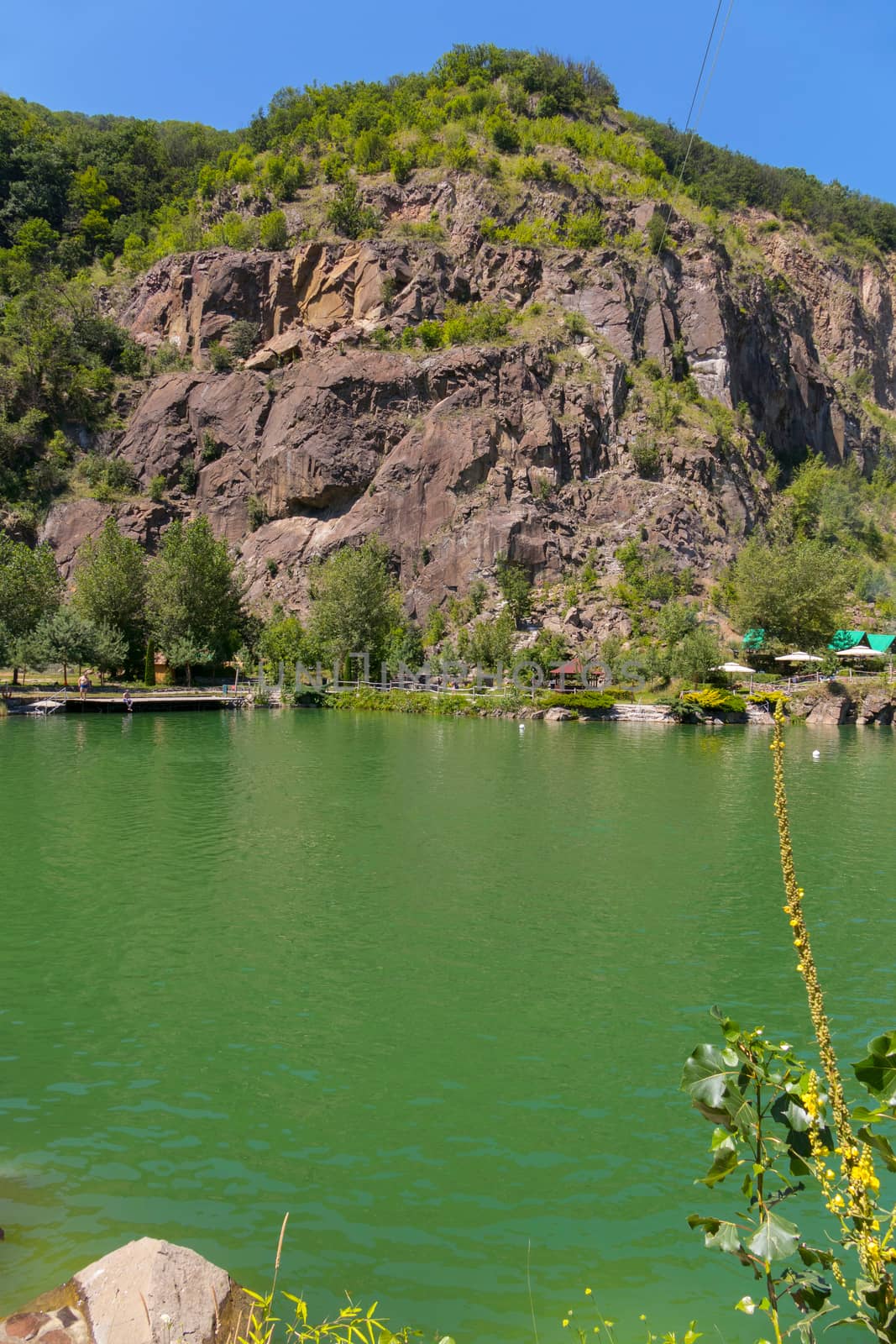 Lake of green water at the foot of the rock with the approach. A place to rest tourists