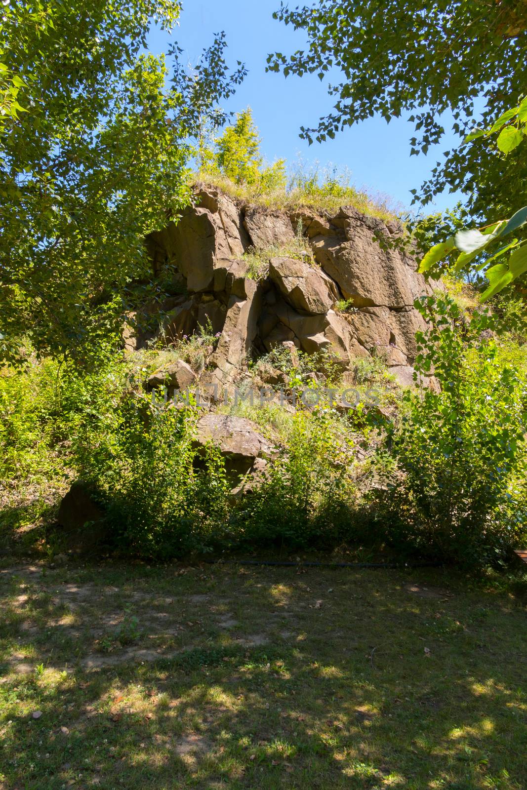 a whimsical form of a slide built of large stones in the shade of trees by Adamchuk