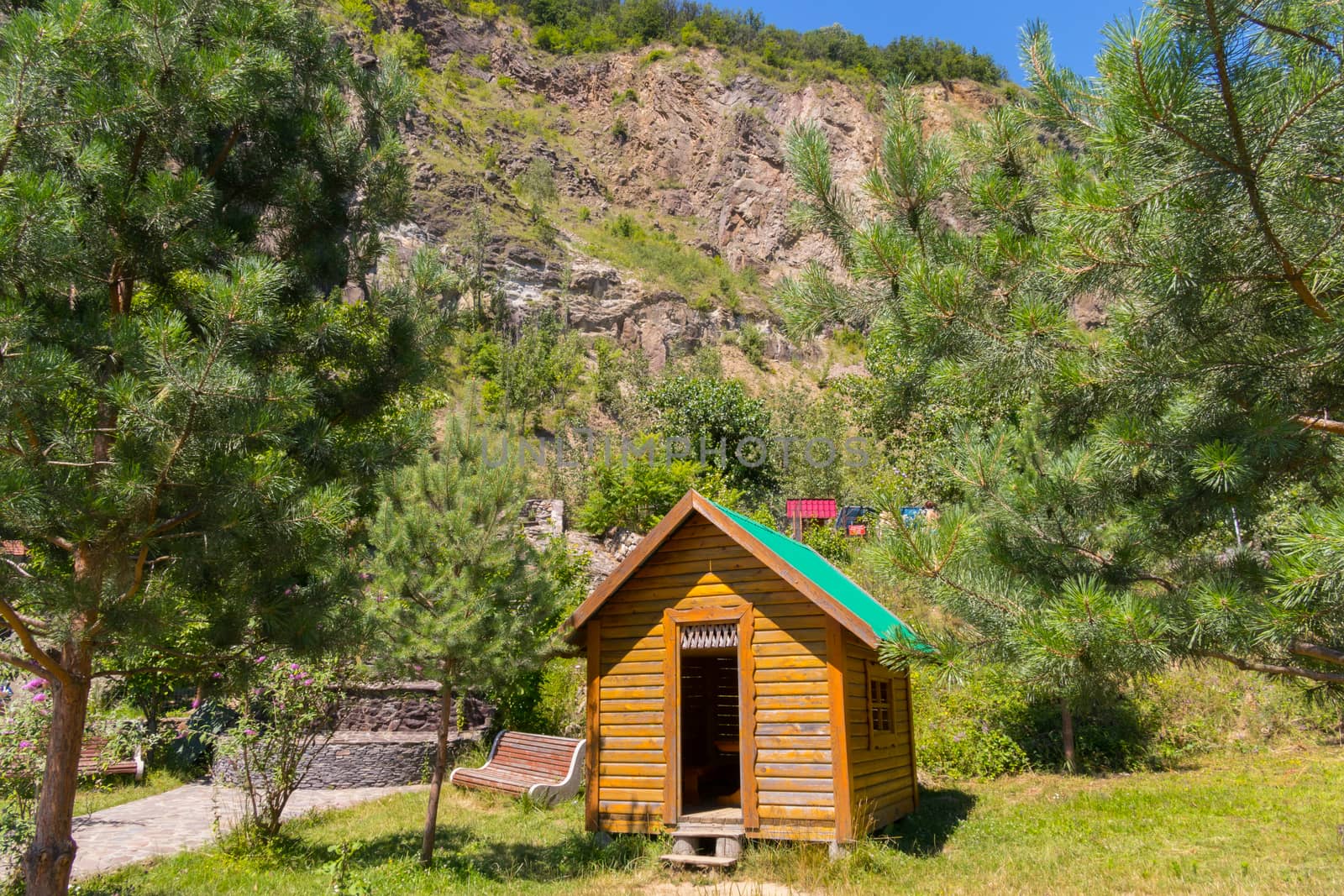 A small wooden house with a green roof on the background of a high rocky mountain