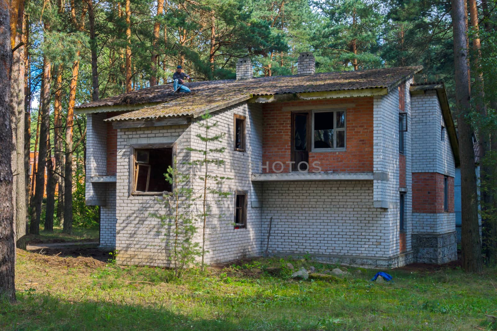 Unfinished brick two-storey house in the background of a pine forest