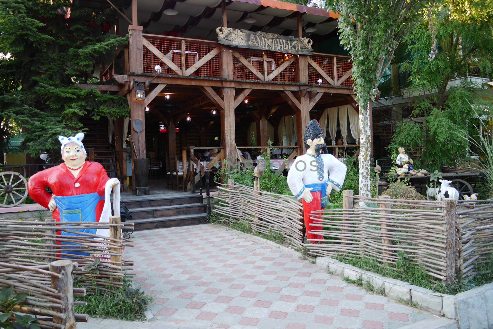 Entrance to the restaurant with heroes of national fairy tales standing in front of him in national clothes with a wicker fence and a wooden cart.