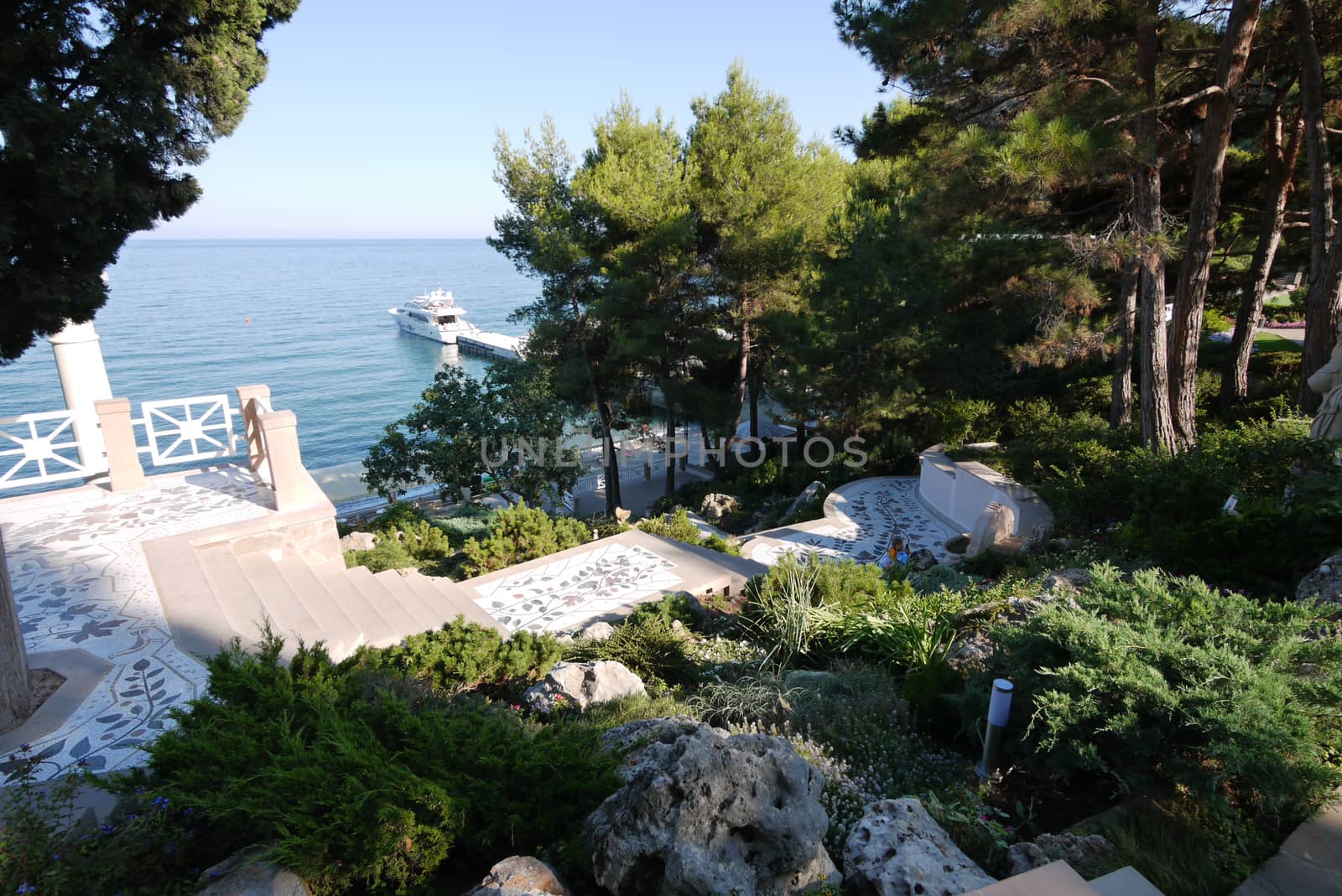 A beautiful view of the embankment with a snow-white boat at the pier. Because of the foliage of trees growing on the shore.