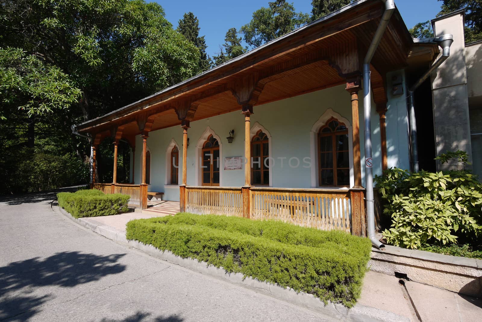 A beautiful veranda with a wooden roof and pillars against the background of the green park zone by Adamchuk