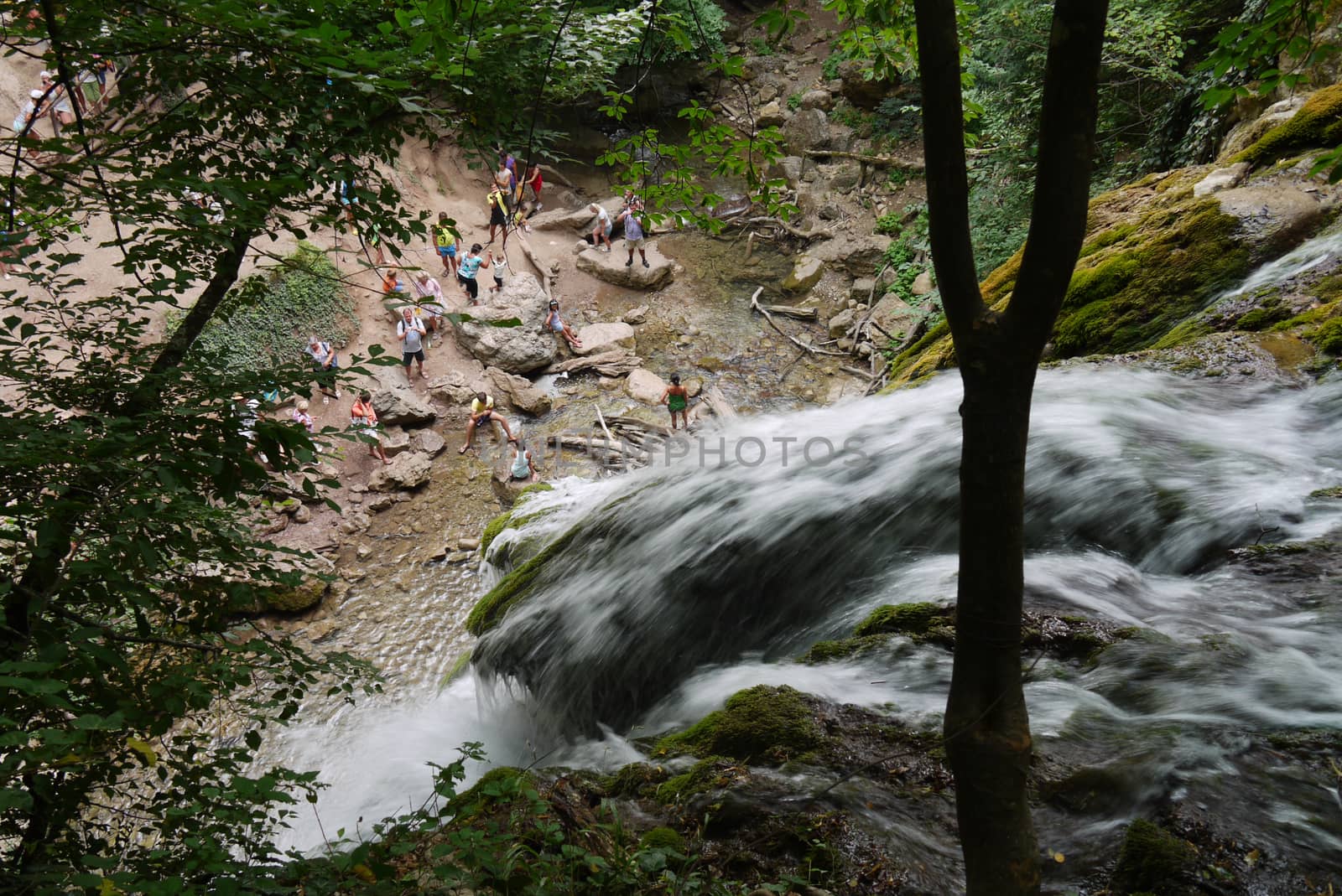 the white foam of a mountain waterfall falls to the foot of the mountain where tourists stand by Adamchuk