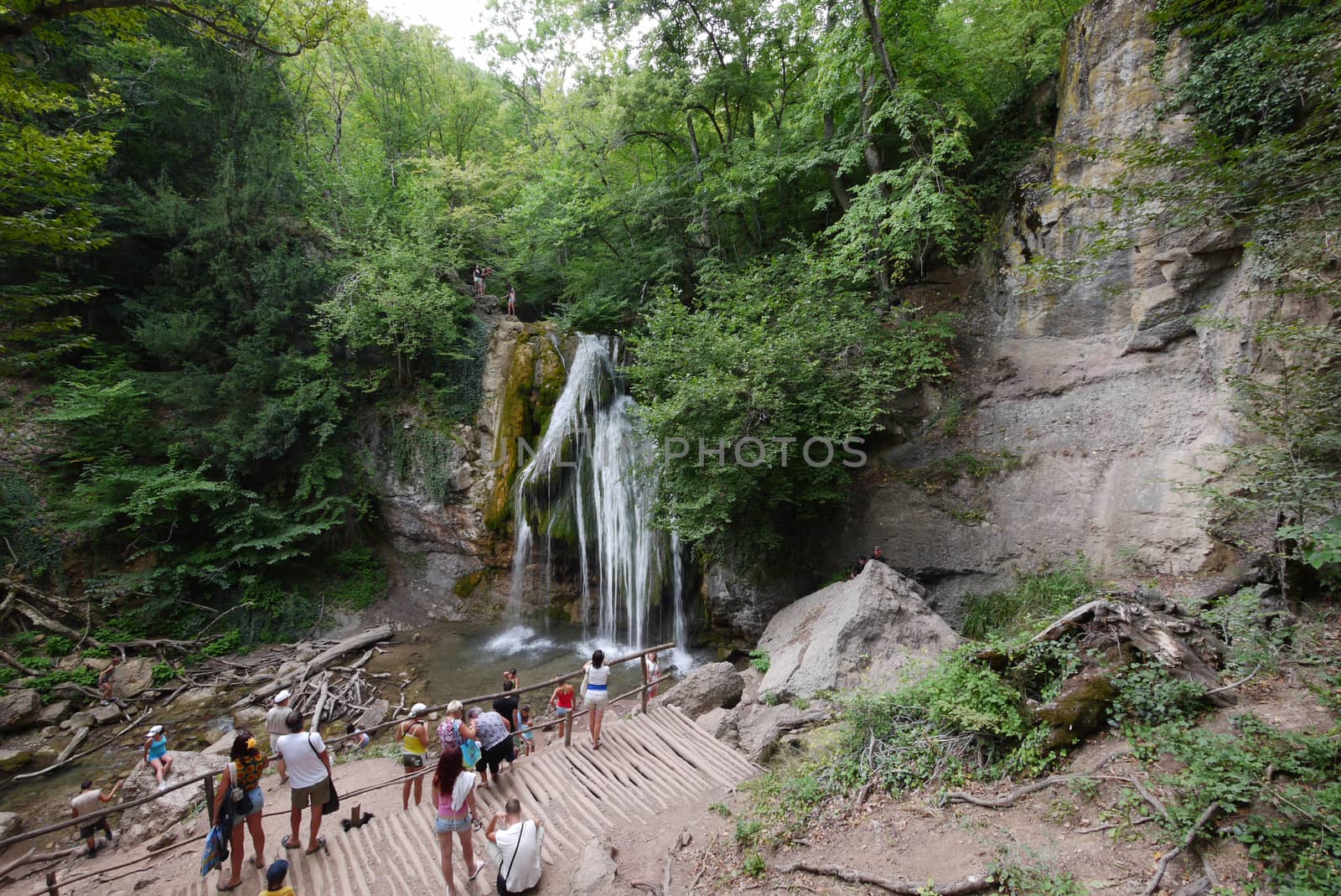 Tourists watch and photograph a beautiful mountain waterfall on a viewing platform near the rocky mountain