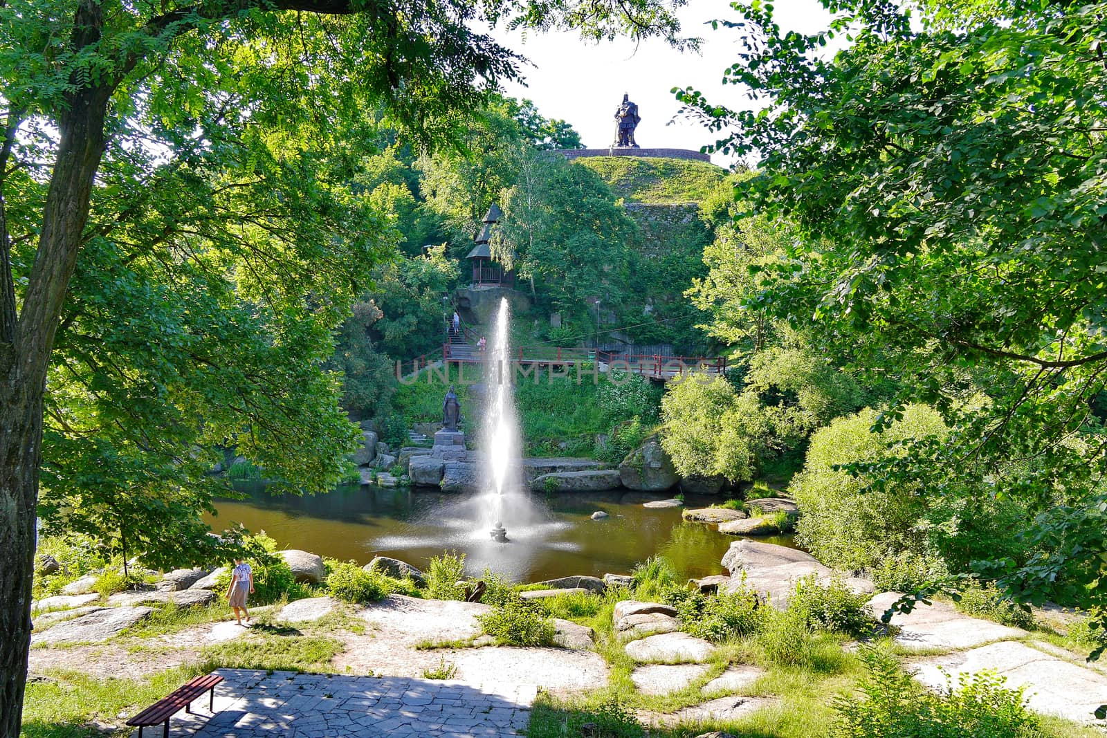 High deorativny fountain in the middle of the lake at the foot of a green hill with a pedestal