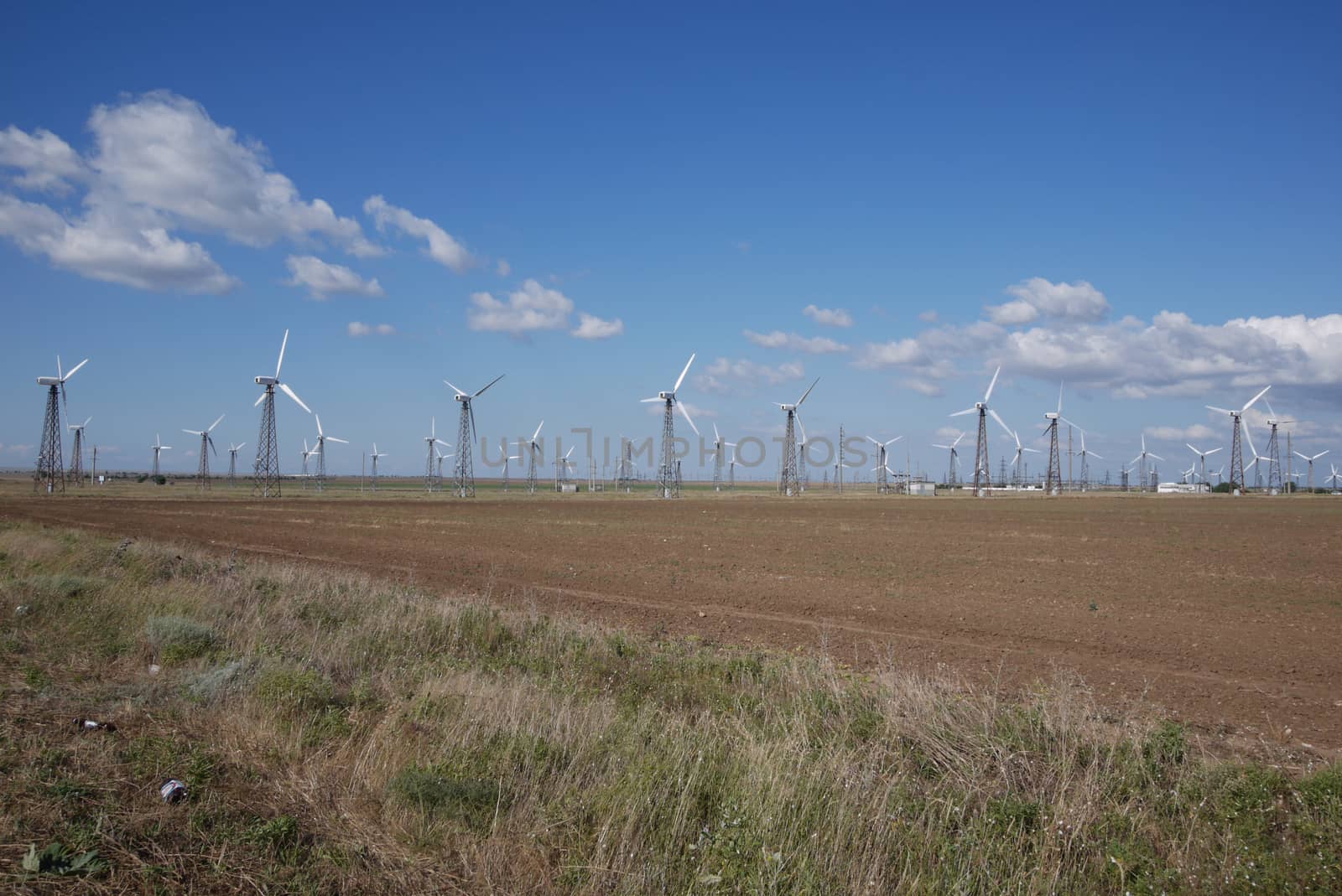 A brown field with a lot of white wind turbines producing electricity