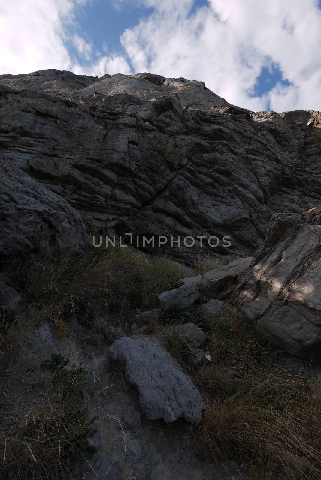 Grassy hollow in a rocky mountain against a blue sky with white clouds