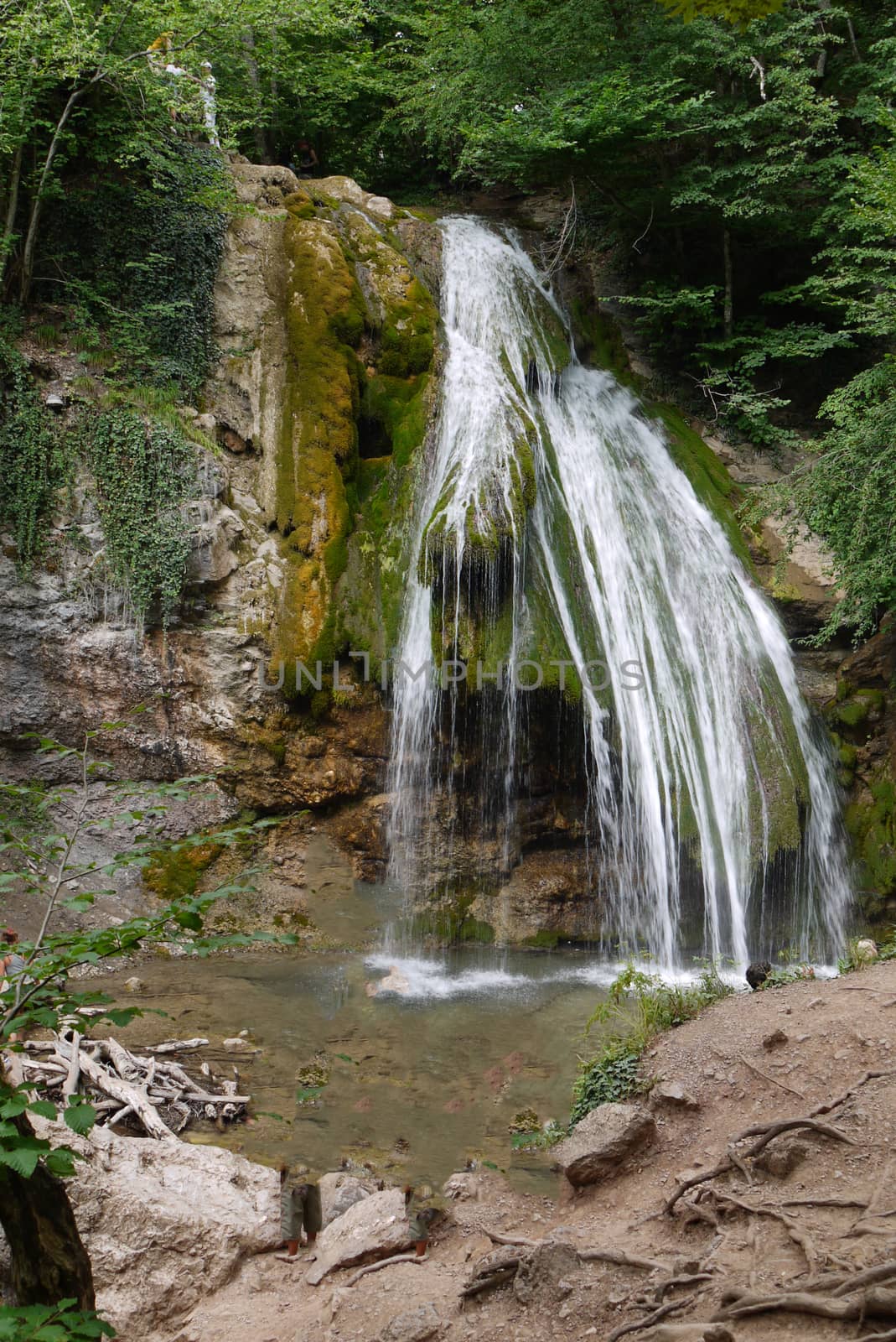 A large picturesque waterfall overgrown with moss and other vegetation falling from a rocky mountain