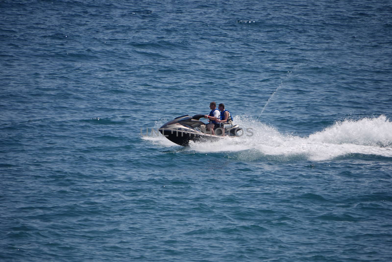 Tourists ride at great speed on a water motorcycle amid the calm waters of the sea. Dressed for safety in life jackets.
