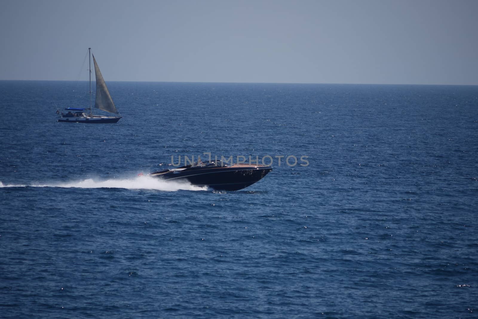 A powerful boat with tourists dissecting the waters of the blue sea and a sailing boat floating nearby.