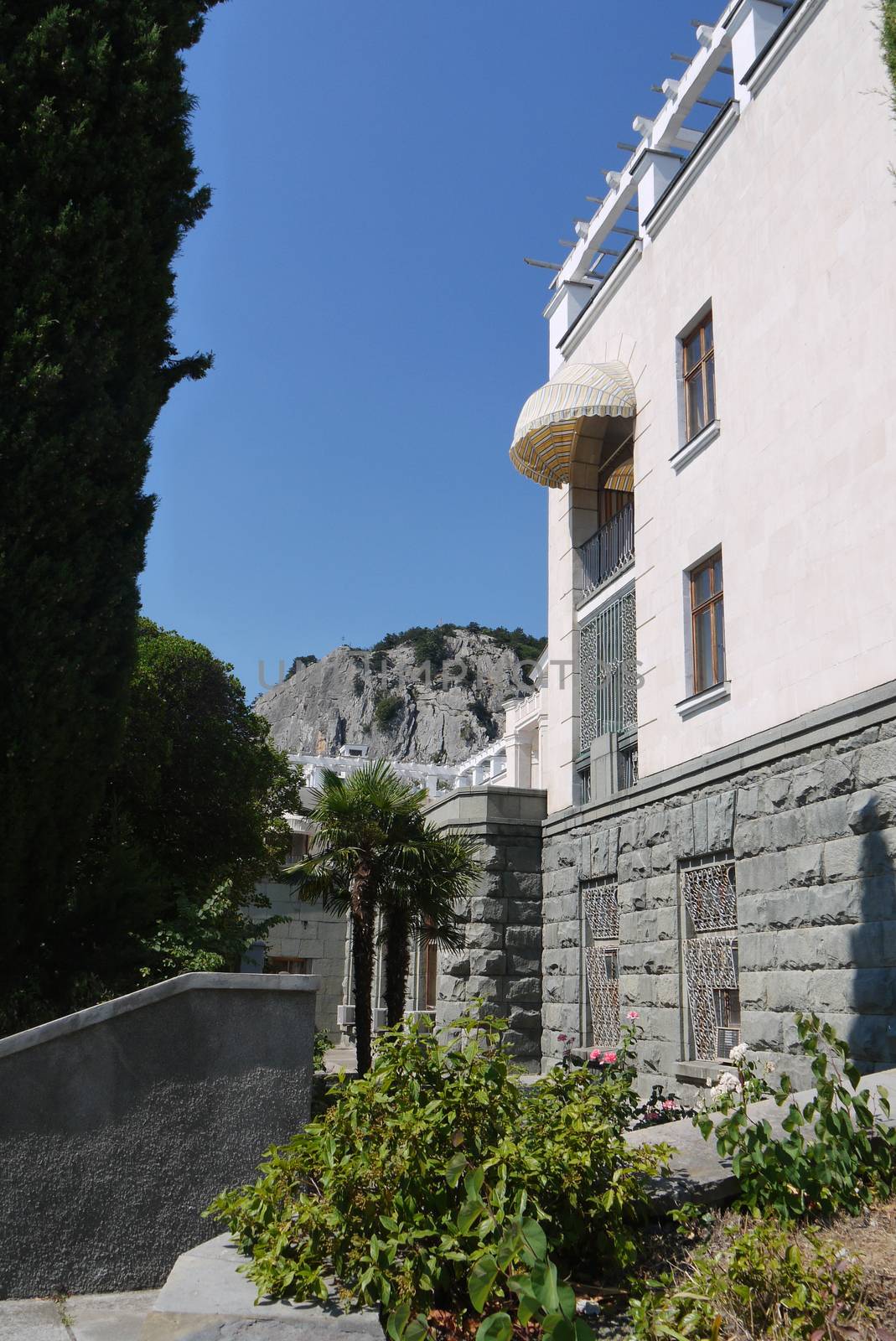 The building of the sanatorium complex with a beautiful balcony and palm trees under it against the background of a high rocky cliff