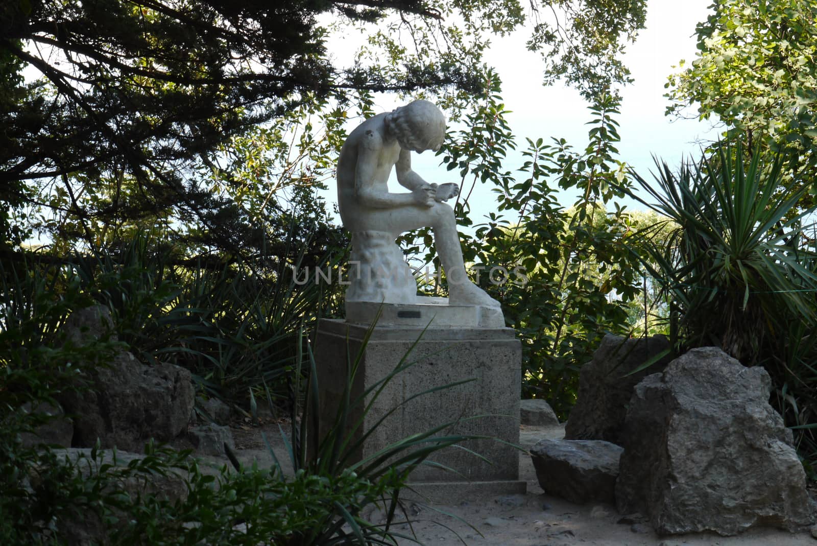 A gypsum white color statue in the shade of a tree among the bushes. It depicts a person writing something to a notebook. by Adamchuk