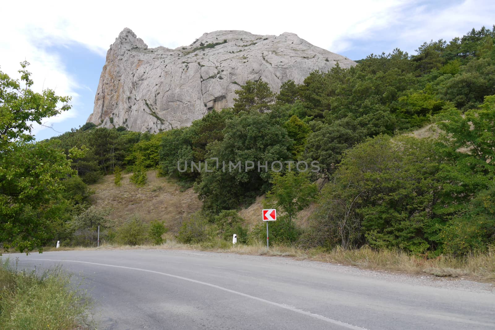 A steep road turn on a background of green vegetation and a high rocky mountain