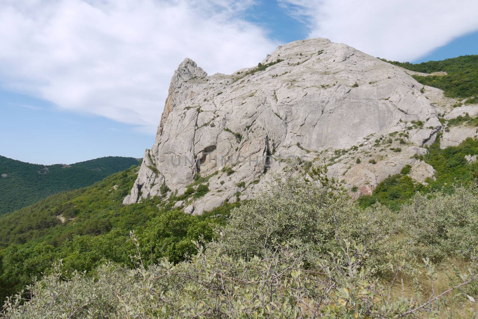 The peak of the rocky mountain against the backdrop of gentle green forests and the endless blue sky