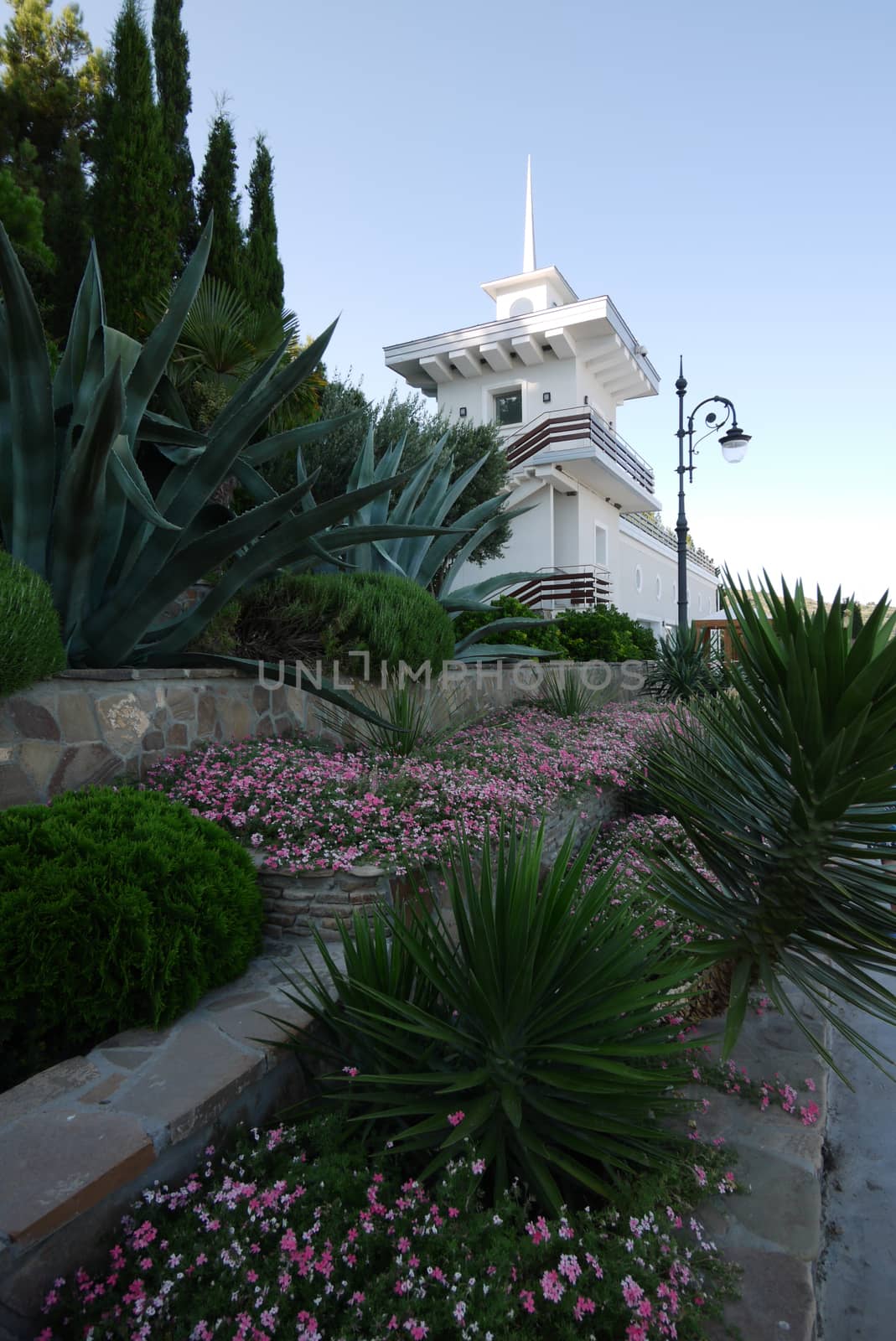 A view from below with a flower bed with flowers on a white building with a peak roof