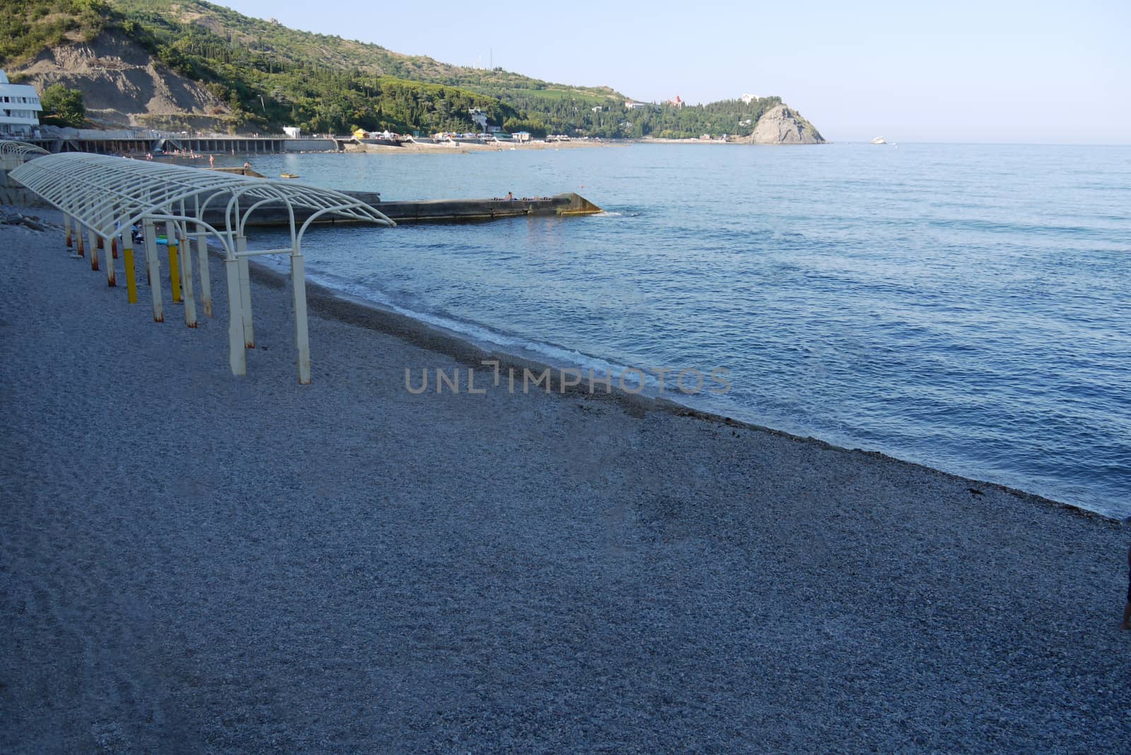 The deserted shore of the beach with a long pier overlooking the sea and a beautiful view of the slopes of the coast opposite with a green scenic nature.