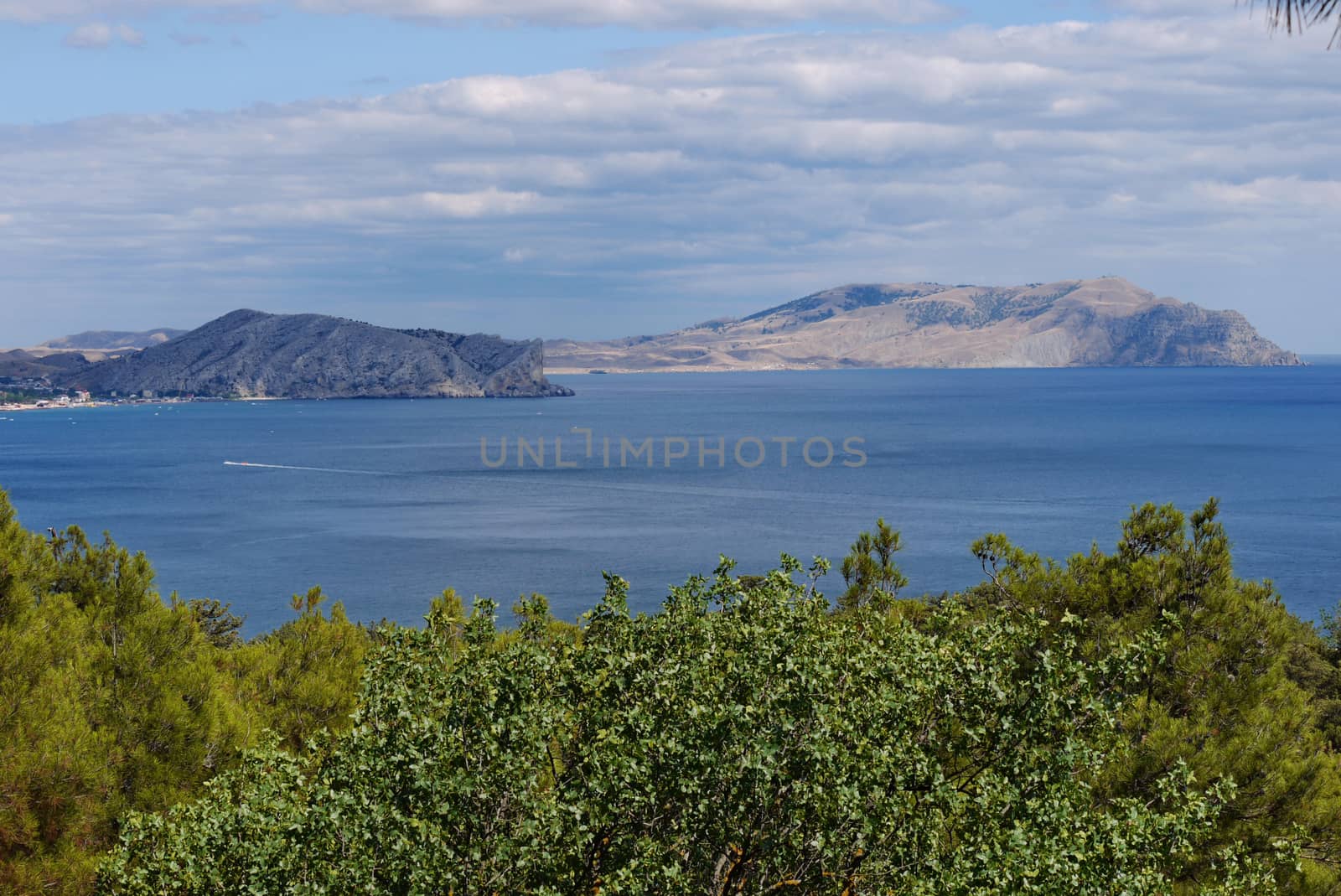 A beautiful landscape of the sea water with a boat sailing in the distance leaving behind a long raging trail among the water surface against the backdrop of high cliffs visible in the distance. by Adamchuk