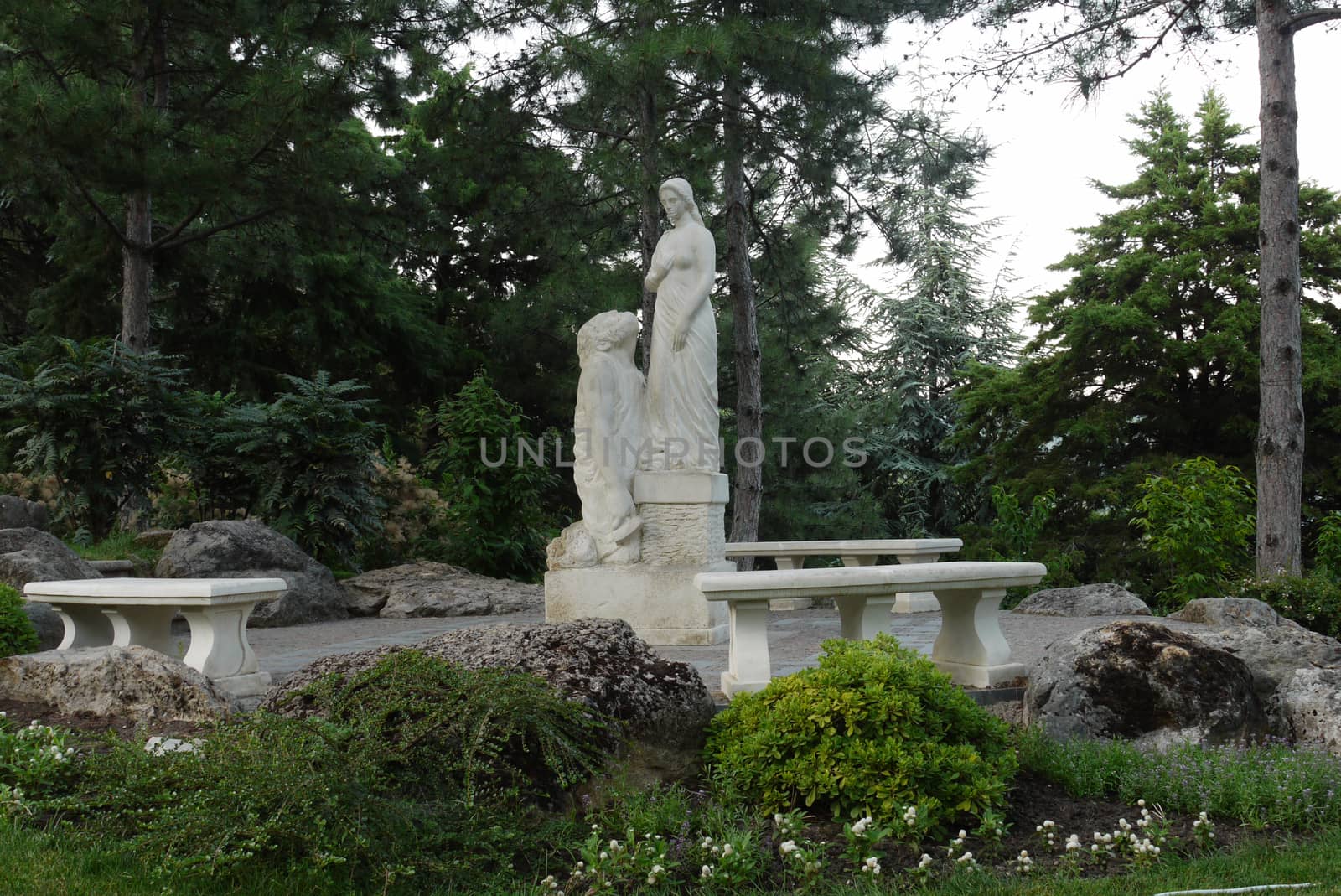 white statue of a frail woman with her husband sculptor on the background of majestic pisoners in the park