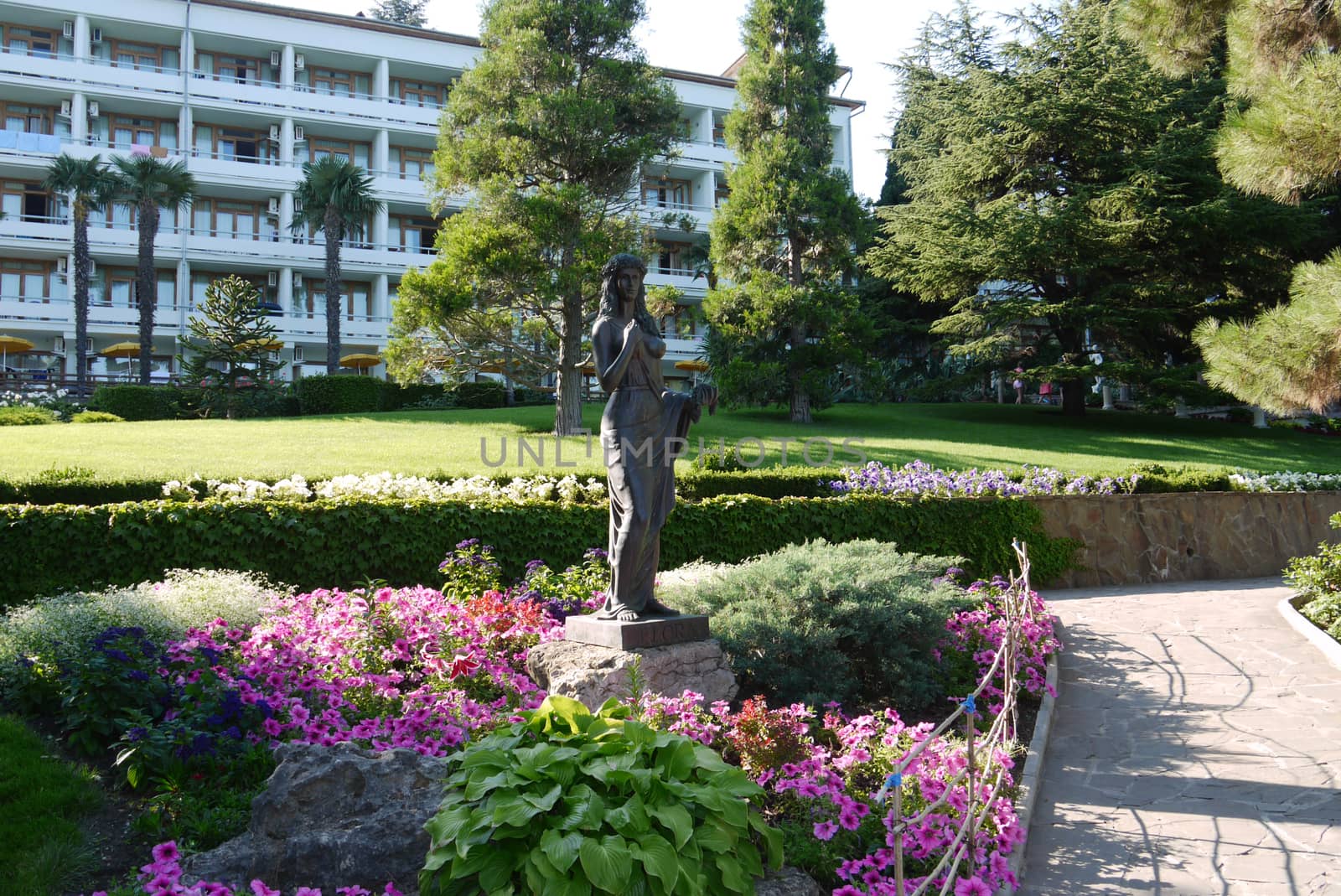 A bronze statue depicting the silhouette of a girl near a flower bed with flowers against the backdrop of a hotel complex by Adamchuk