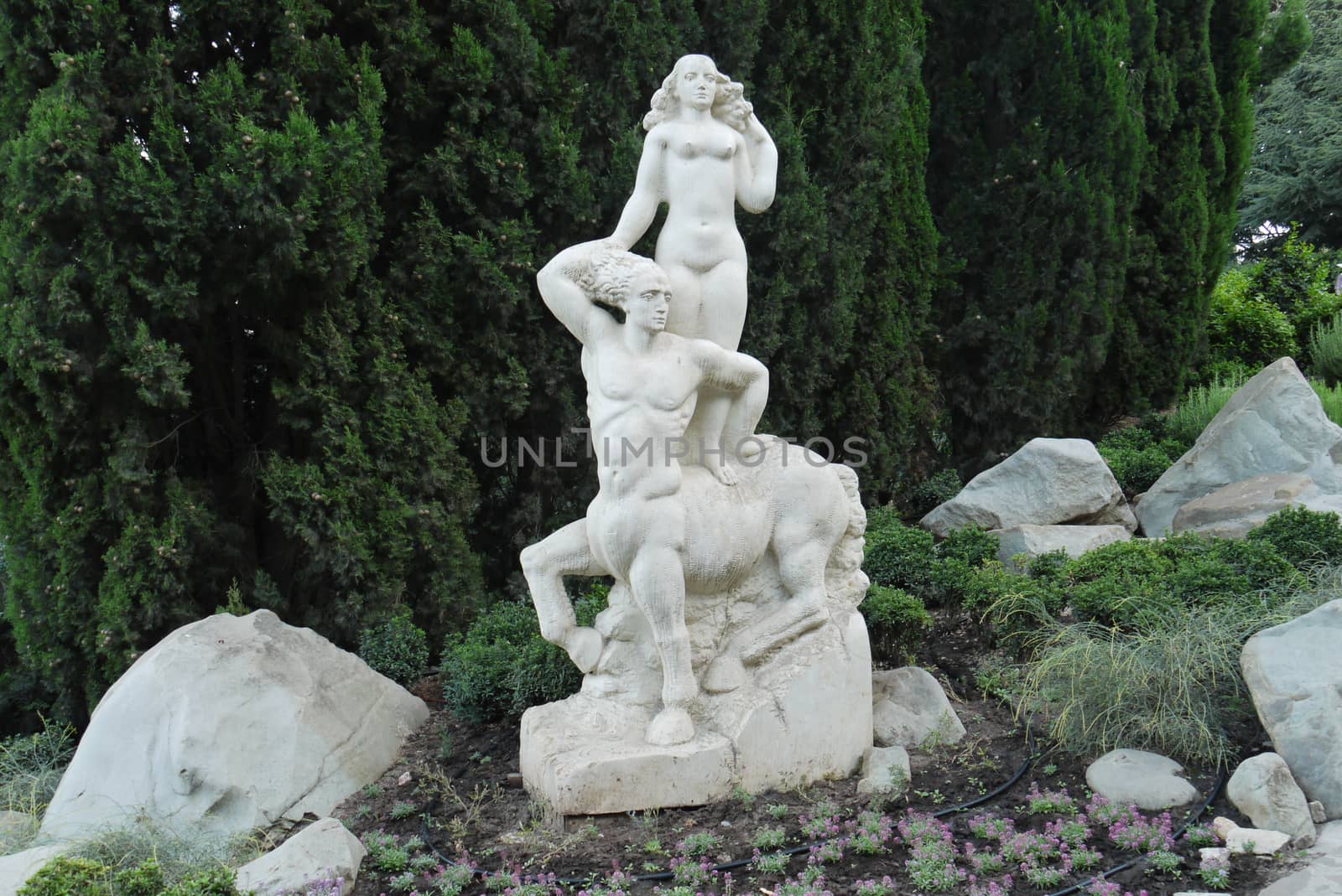 A white statue of a woman at a centaur against a background of green tuy in the park