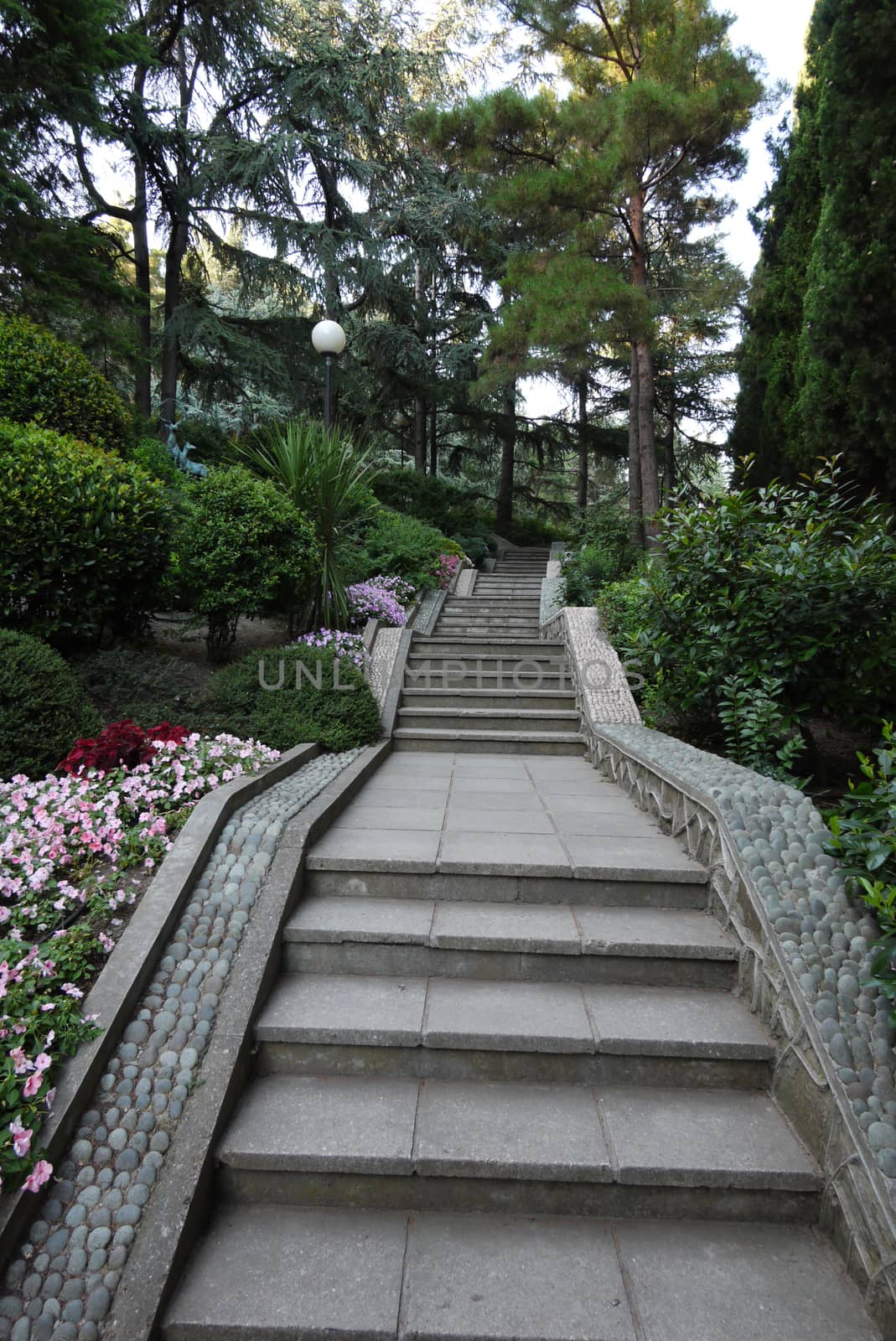 alley with stone staircases and lanterns in a park with green trees by Adamchuk