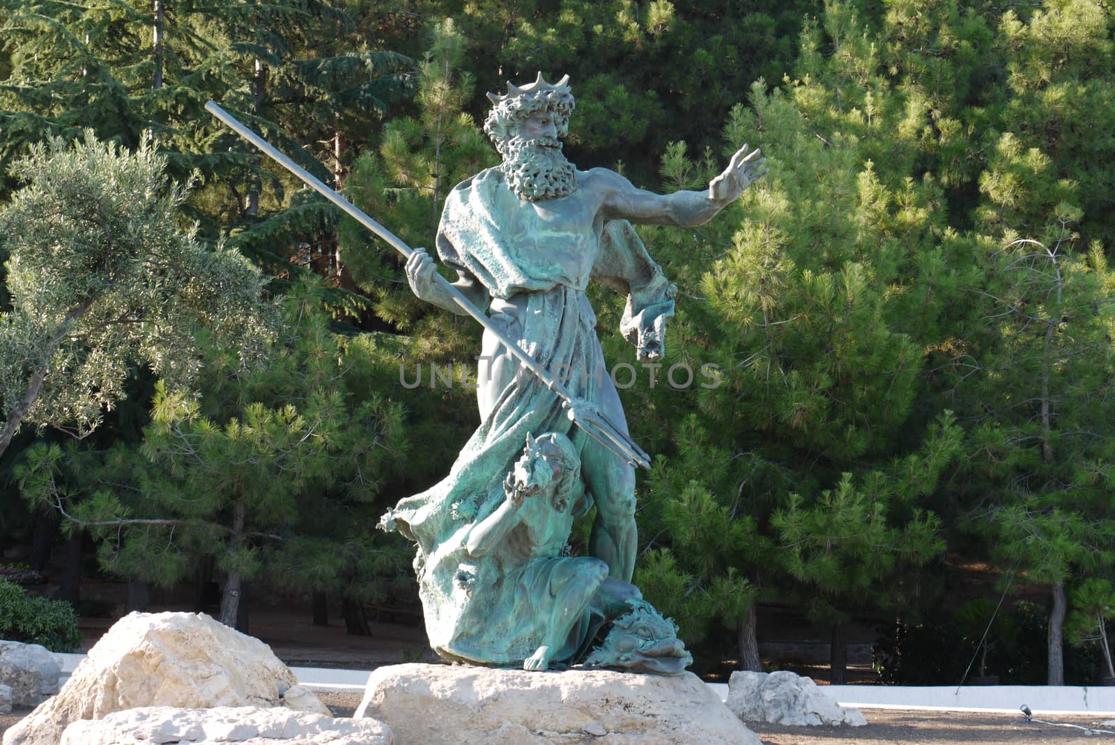 Sculpture of Neptune with a spear on a stone in the background of a coniferous park