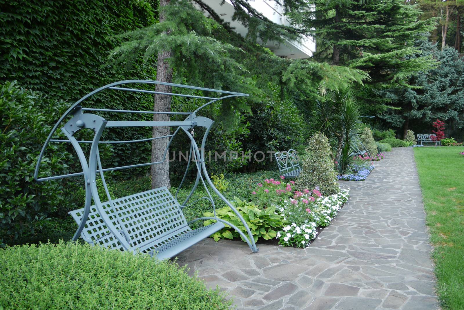 Decorative green pendant bench on the background of a walking park area with alleys and beautiful plantings