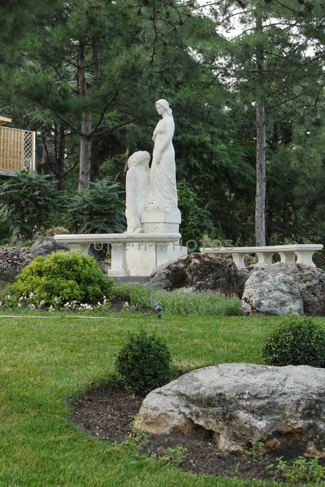 A tall sculpture standing on a white pedestal in a park next to  by Adamchuk