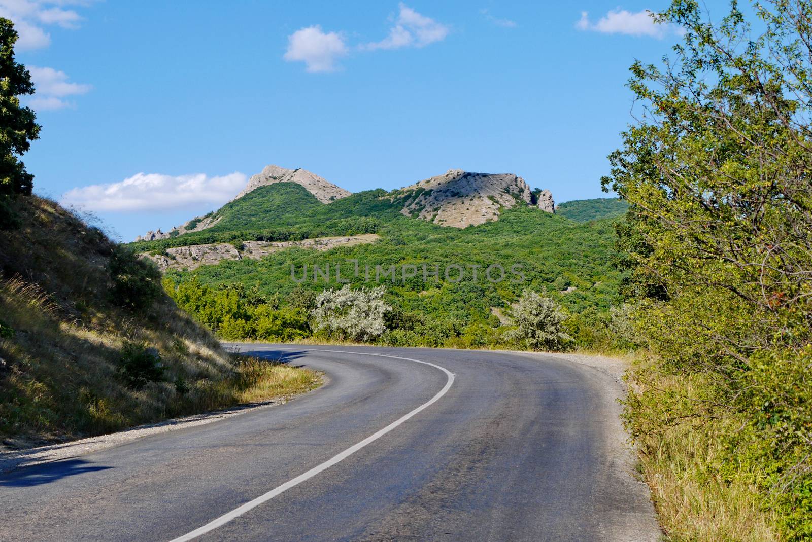 the road is rolled up against the background of high cliffs covered with grass under the blue sky by Adamchuk