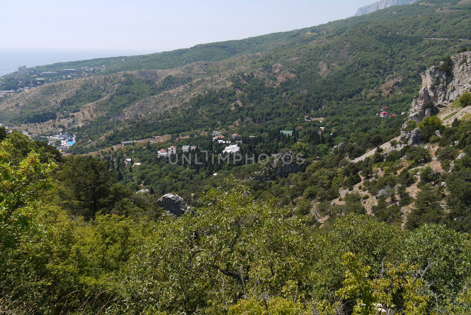 A small cozy village surrounded by forest covered with mountains on the background of a wide Black Sea by Adamchuk