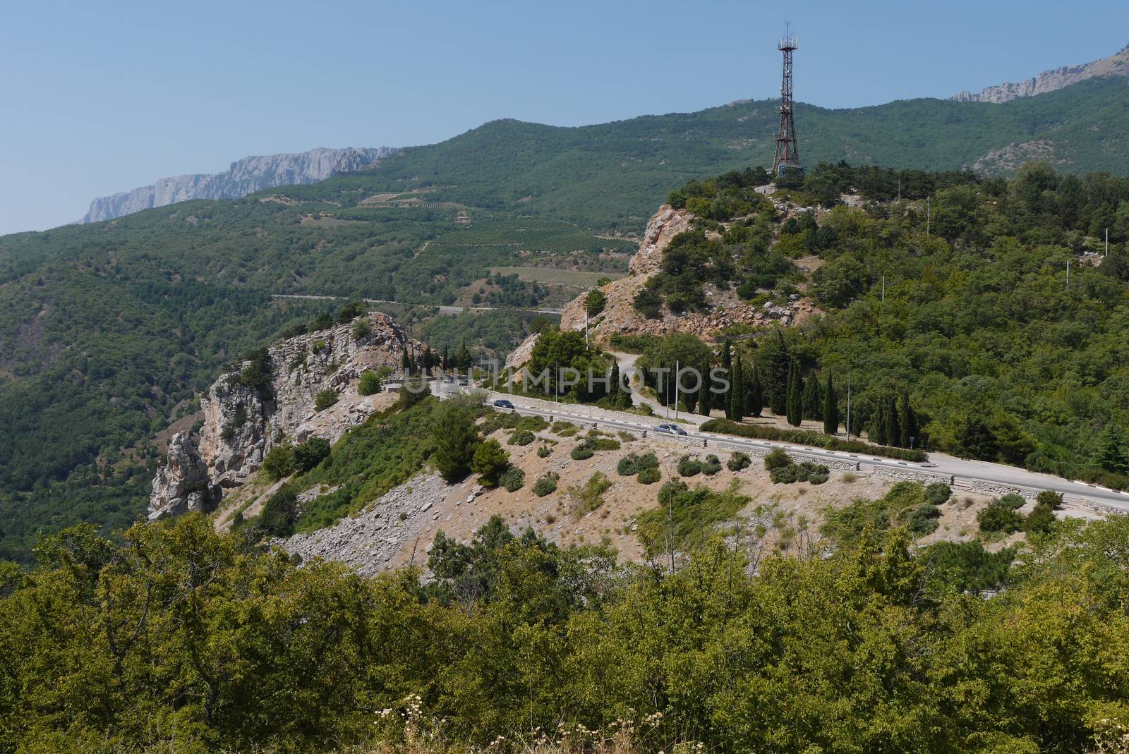 the rocky road is rolled up against the background of high mountains covered with trees