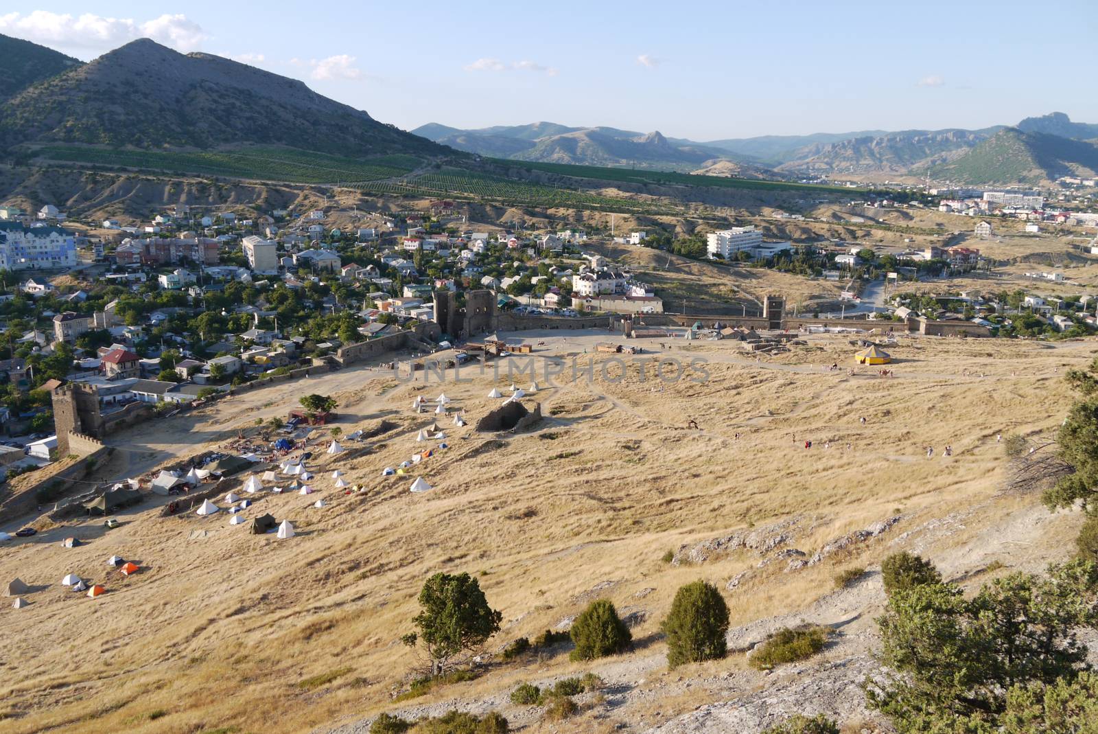 a small cozy town surrounded by high grassy slopes on a blue sky background