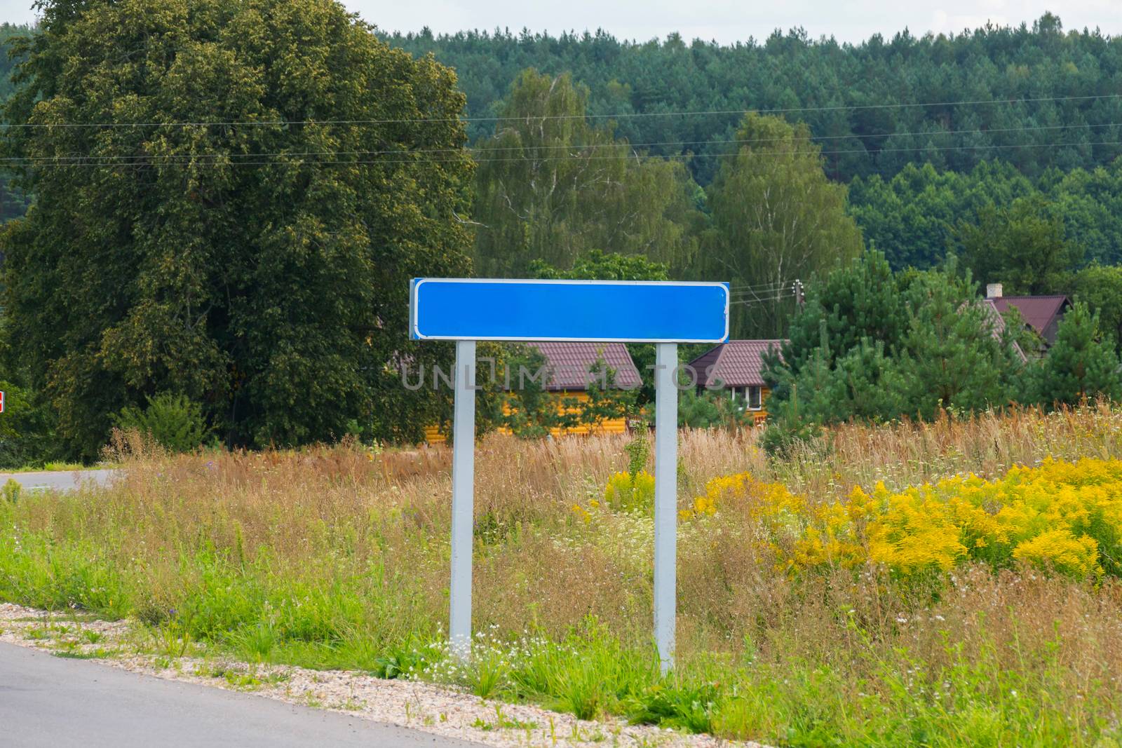 An empty road sign on the background of houses surrounded by trees