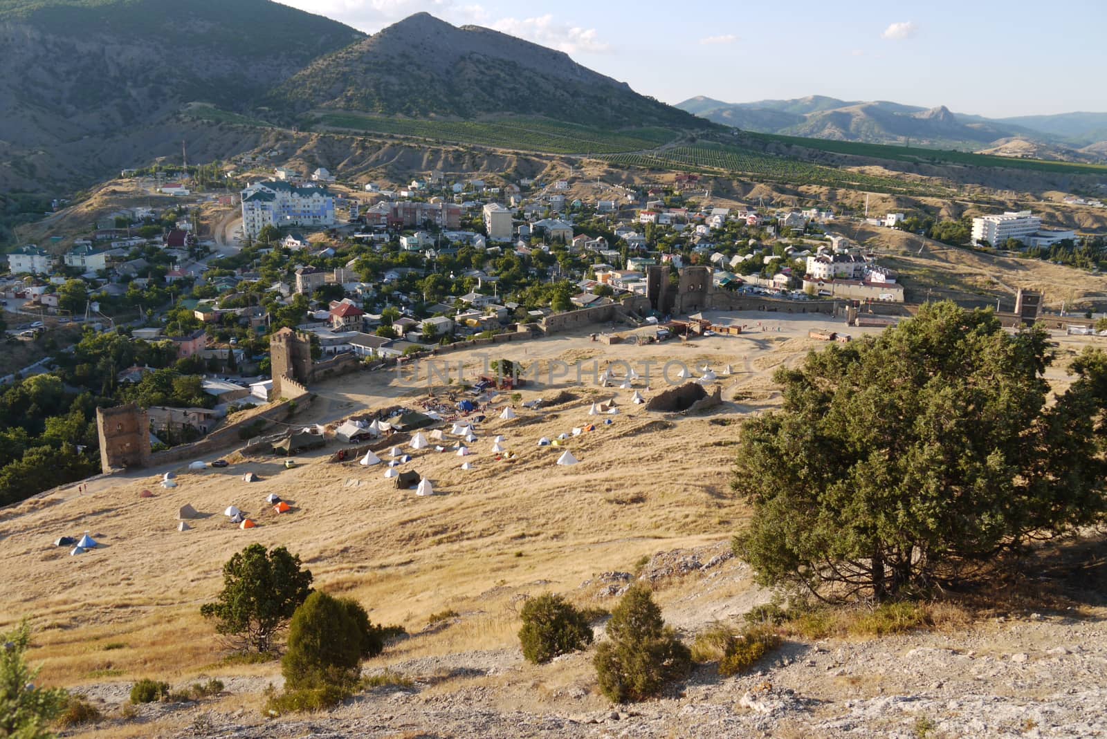 a small cozy town surrounded by high grassy slopes on a blue sky background by Adamchuk