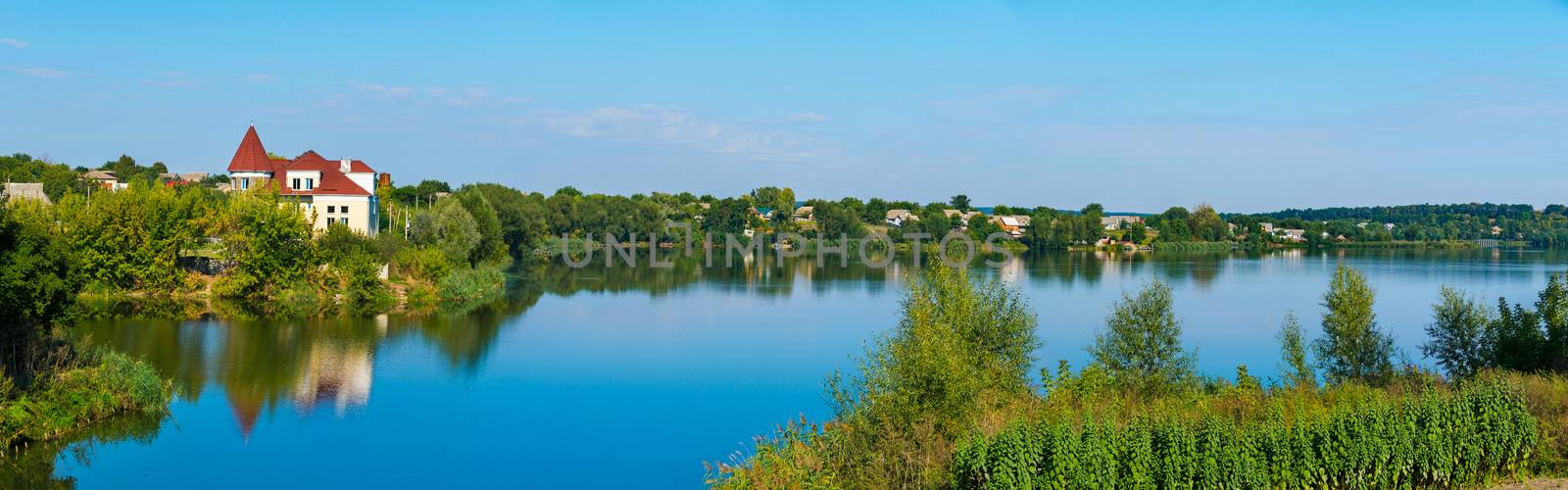 a small settlement under a blue sky on the shores of a wide deep lake