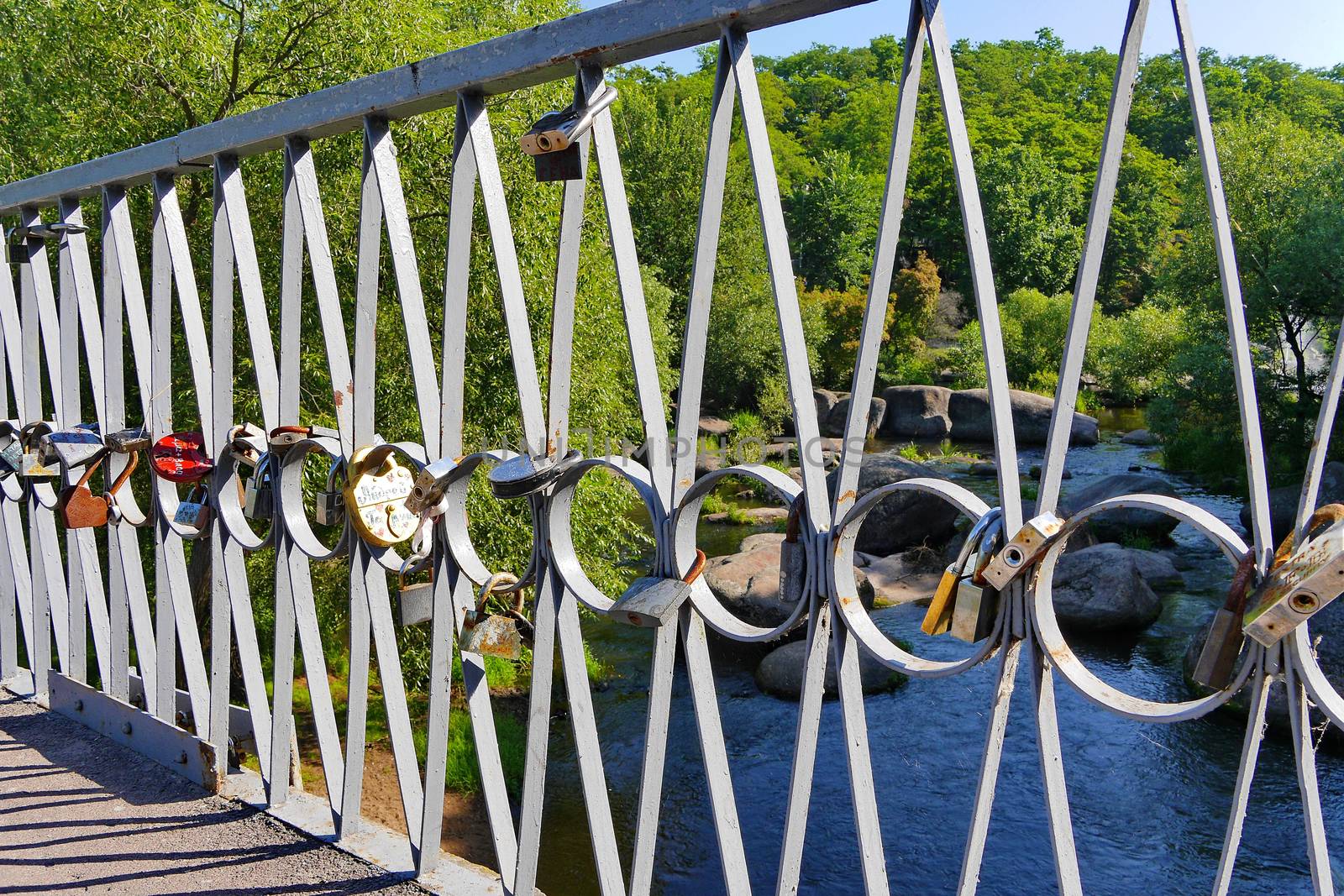 a love bridge on the background of a rocky river surrounded by dense trees by Adamchuk