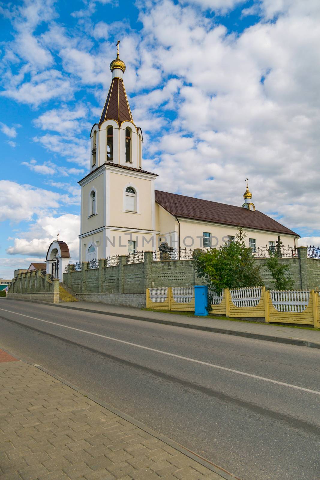 a small church surrounded by a high fence against a cloudy blue sky by Adamchuk