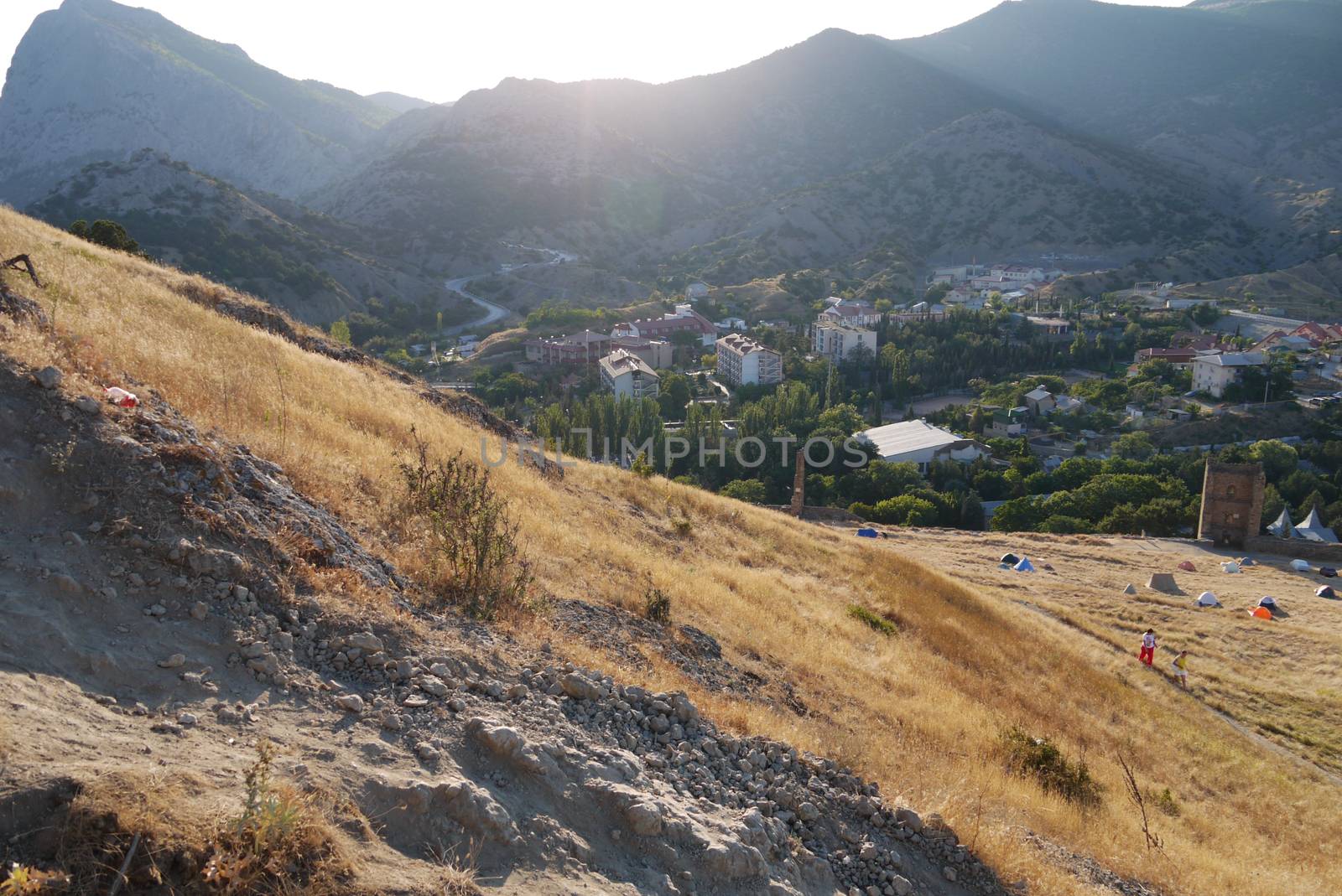 sandy slopes on the background of a cozy town and high mountains covered with grass by Adamchuk