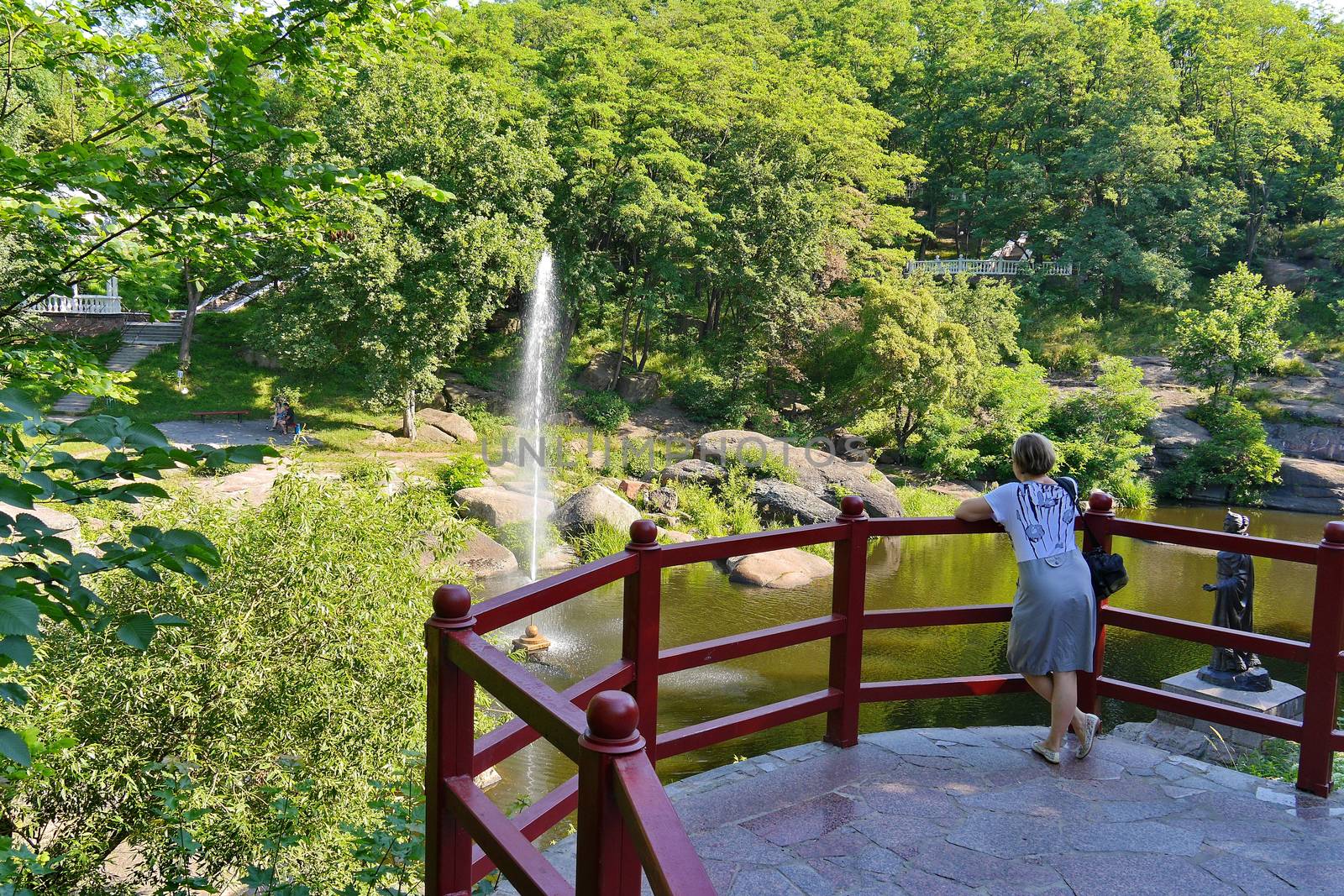A panoramic view of the rocky river and the fountain surrounded by tall, lush trees