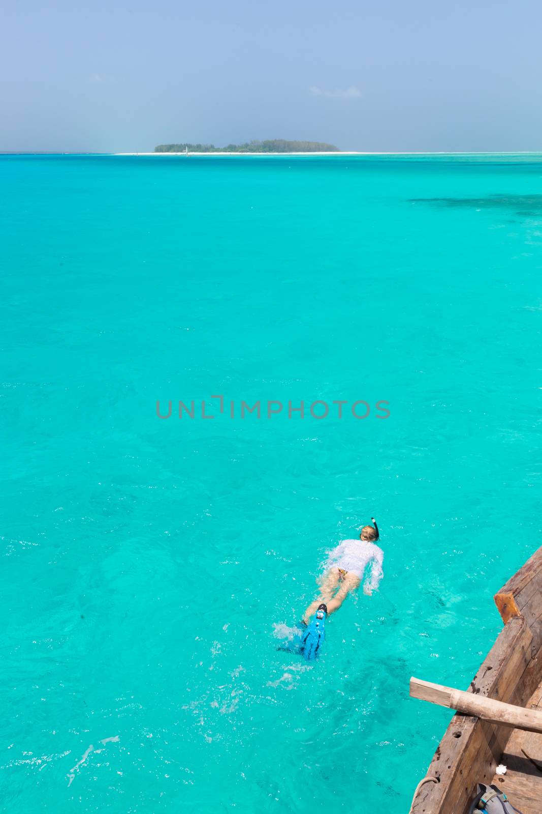 Woman snorkeling in clear shallow sea of tropical lagoon with turquoise blue water and coral reef, near exotic island. Mnemba island, Zanzibar, Tanzania.