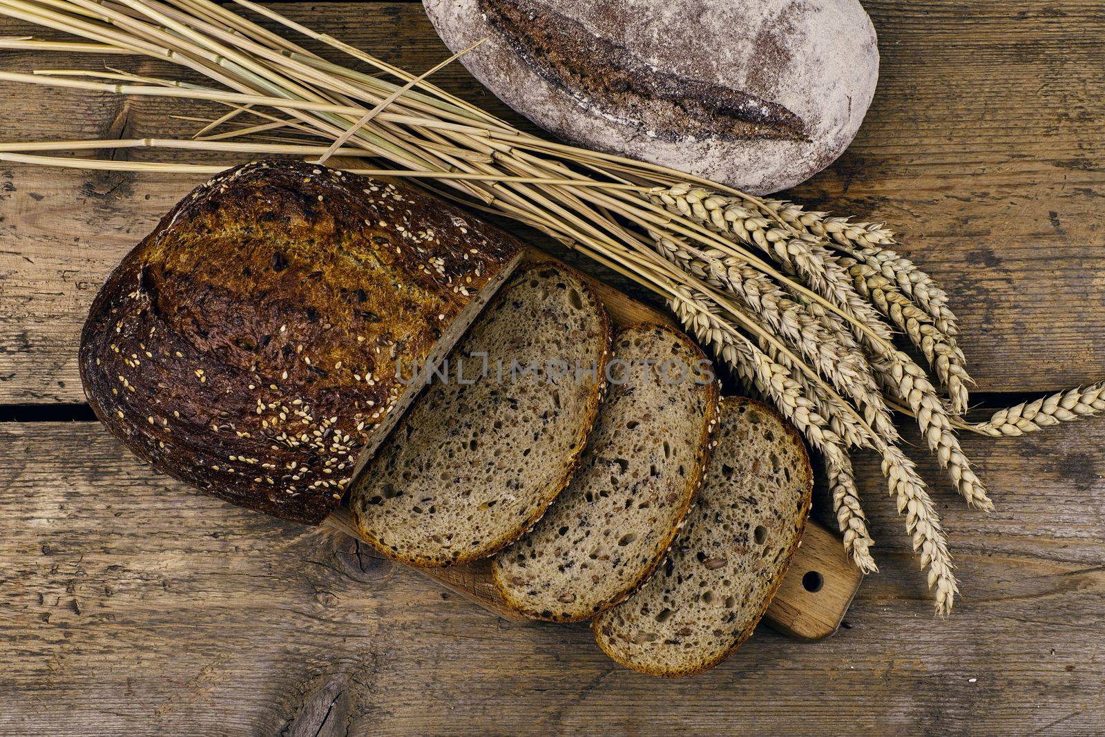 Loafs of bread, slices of bread and ears of grain on wood background. Rustic and rural concept. Close up.  