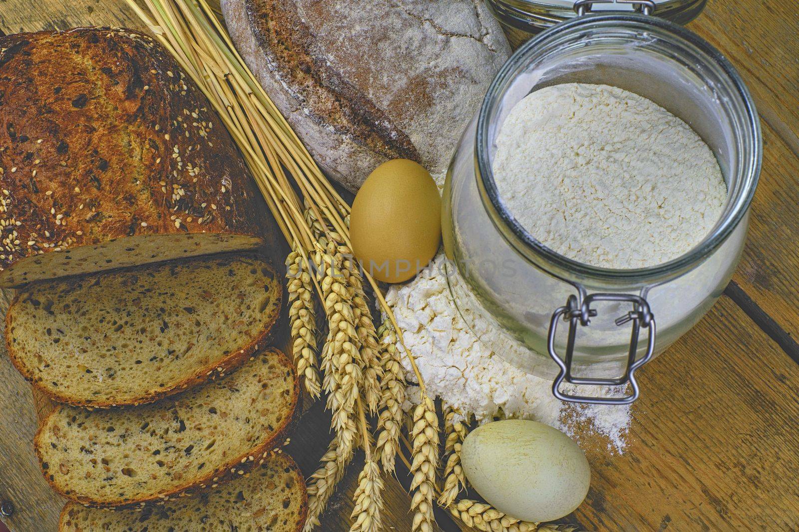 Loafs of bread, slices of bread, wheat flour, eggs and ears of grain on wood background. Rustic and rural concept. Close up. Flat lay.  